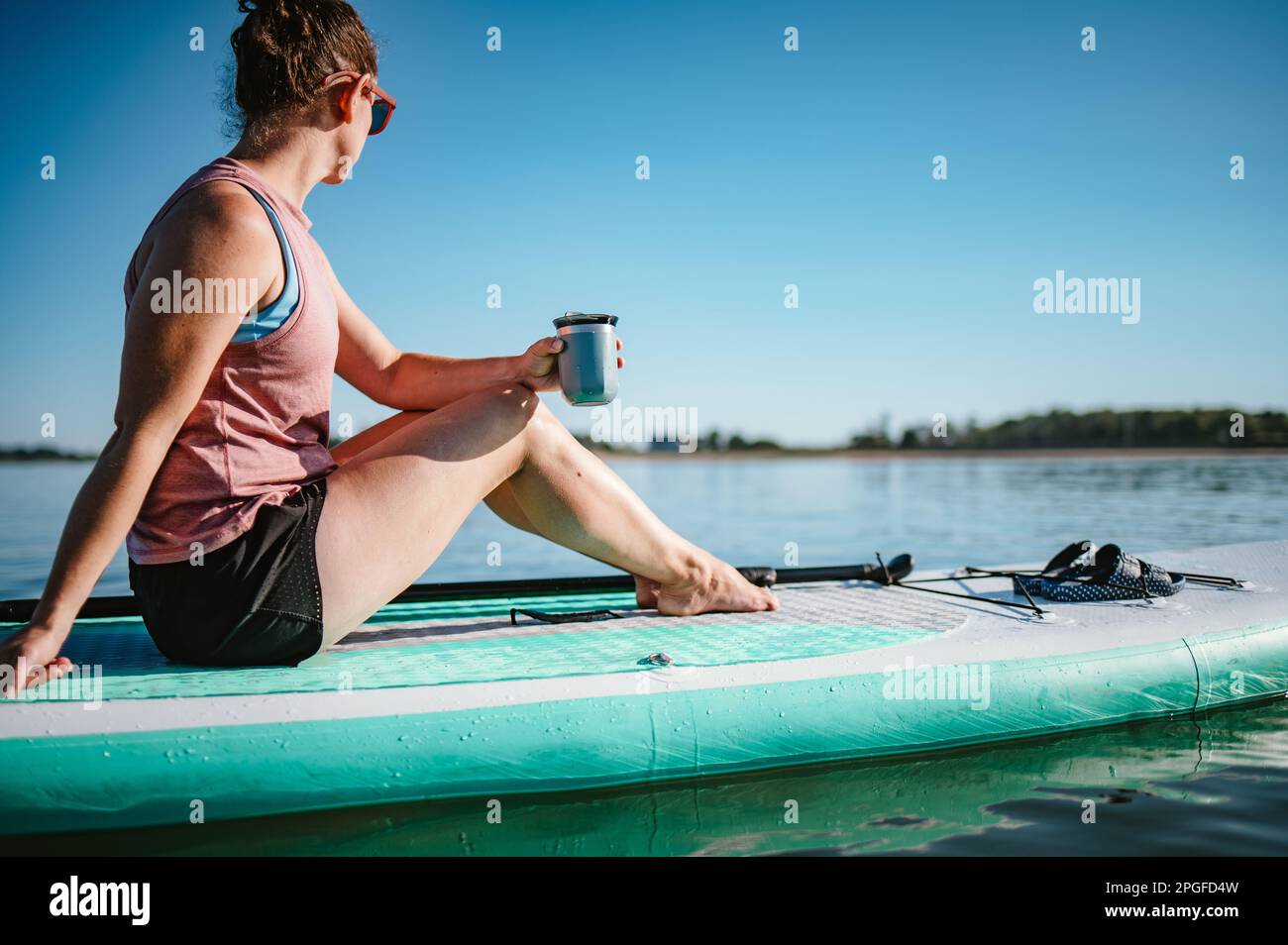 Eine Frau, die aus einem Becher auf einem Stand-up-Paddleboard auf dem Meer trinkt Stockfoto