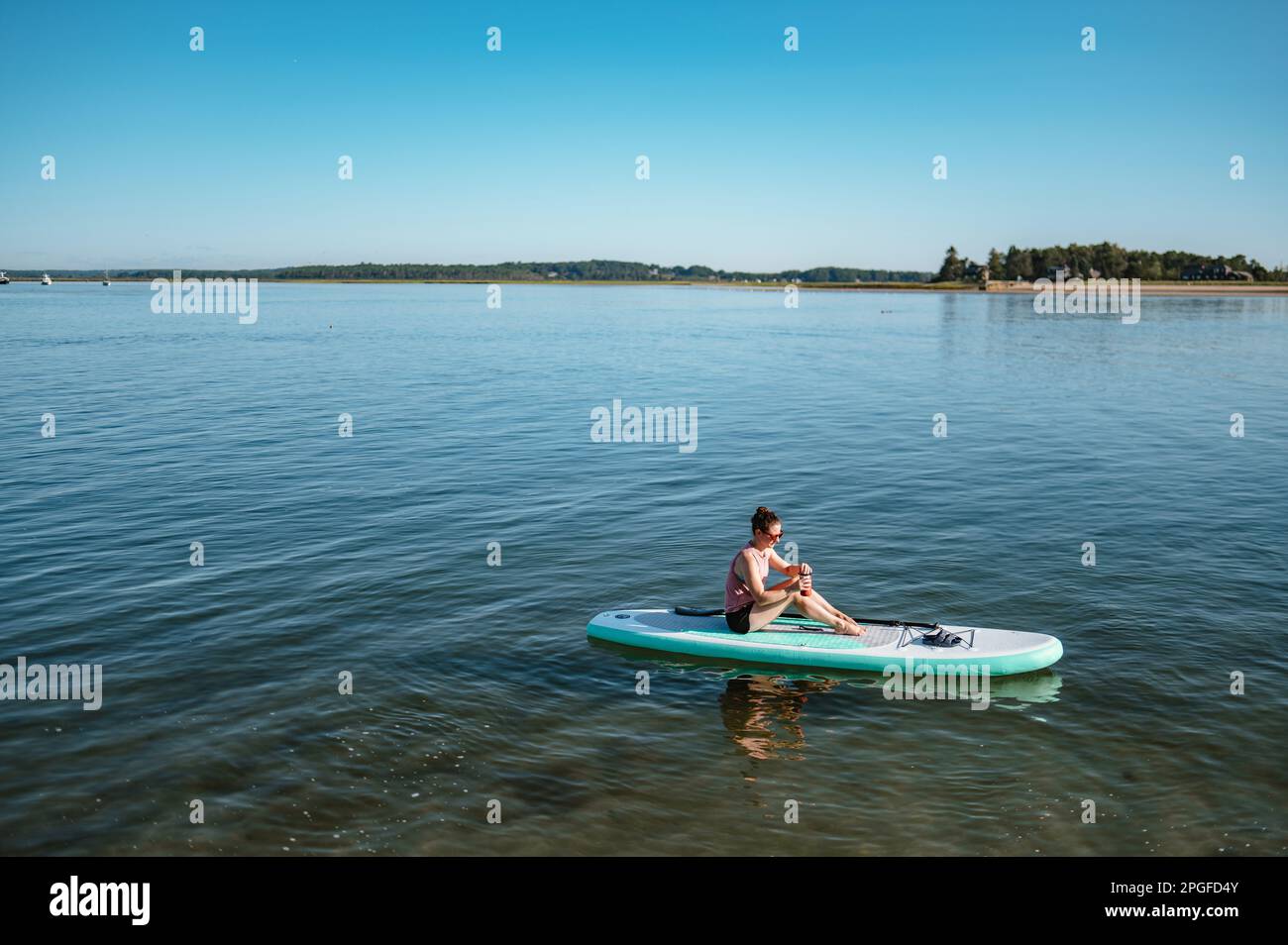 Eine Frau, die aus einem Becher auf einem Stand-up-Paddleboard auf dem Meer trinkt Stockfoto