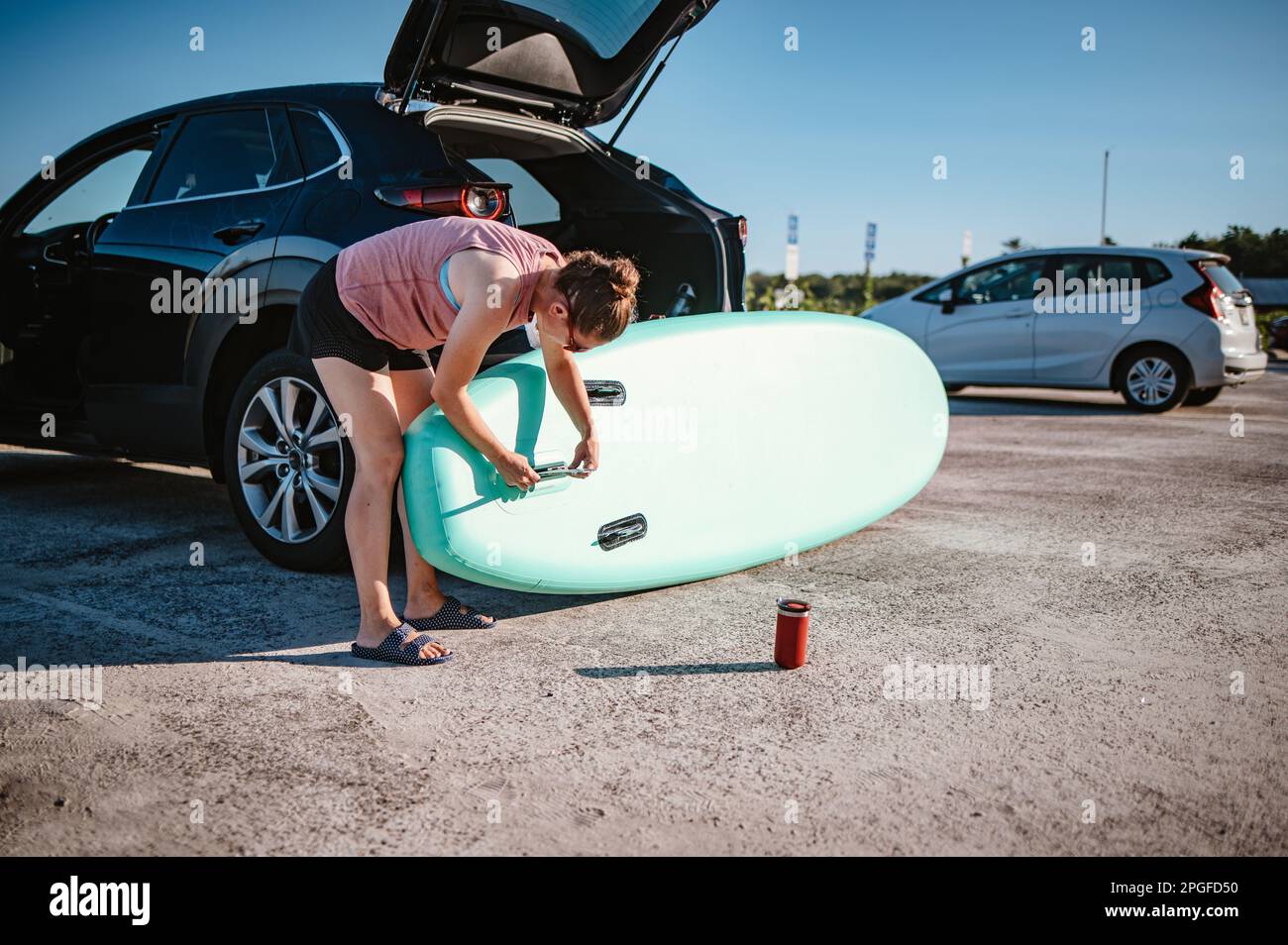 Eine Frau, die hinter ihrem Auto ein Stehpaddleboard zusammenbaut Stockfoto