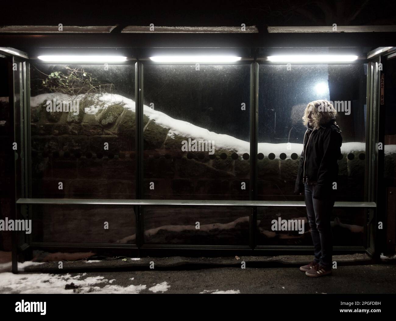Farbbild einer Frau, die im Winter an einer Bustop wartet Stockfoto