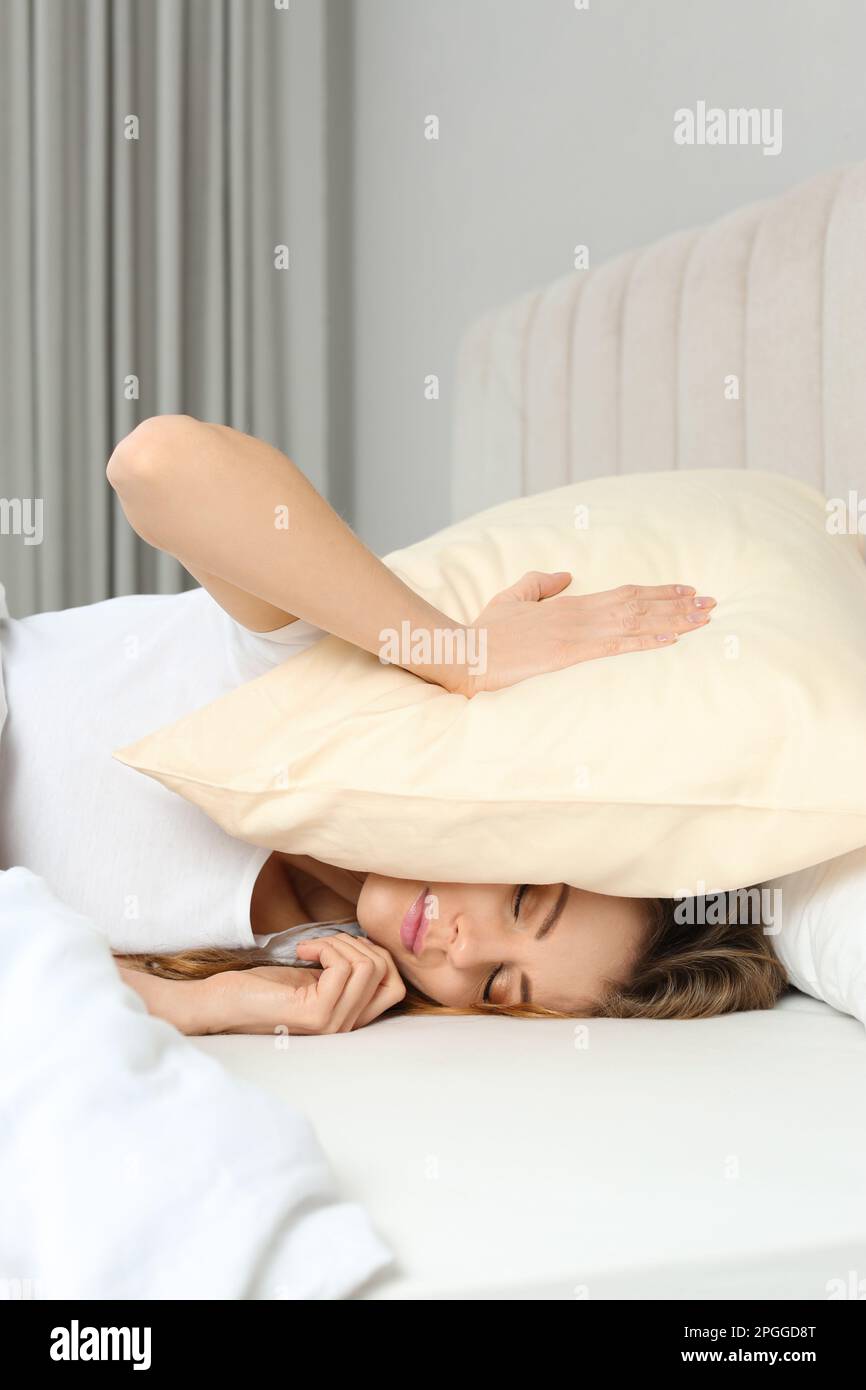 Schlaflose Frau, die zu Hause den Kopf mit einem Kissen im Bett bedeckt Stockfoto