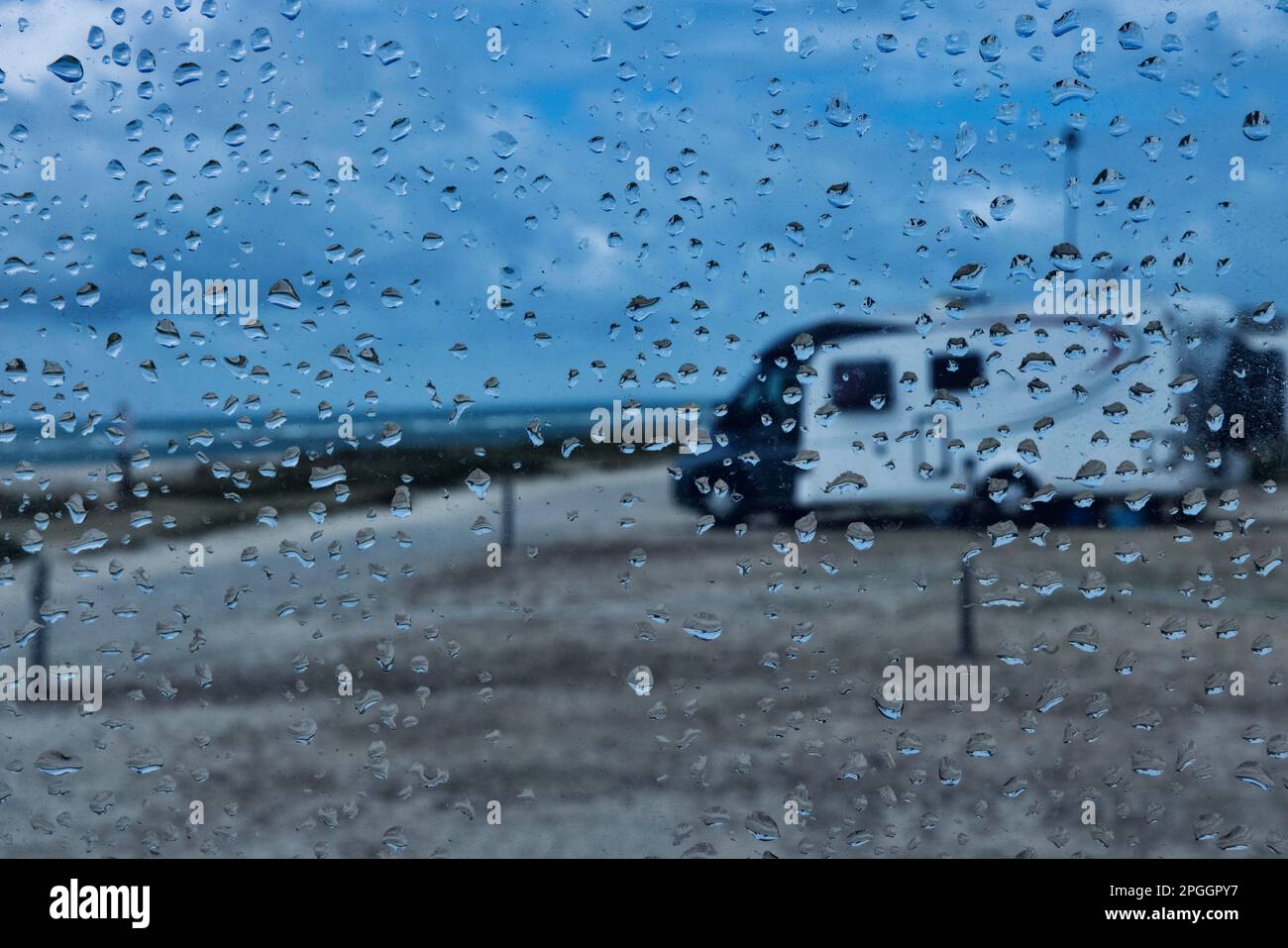 Blick durch ein Fenster mit Regentropfen in einem Wohnmobil auf einem Campingvan am Meer, Portbail, Normandie, Frankreich Stockfoto