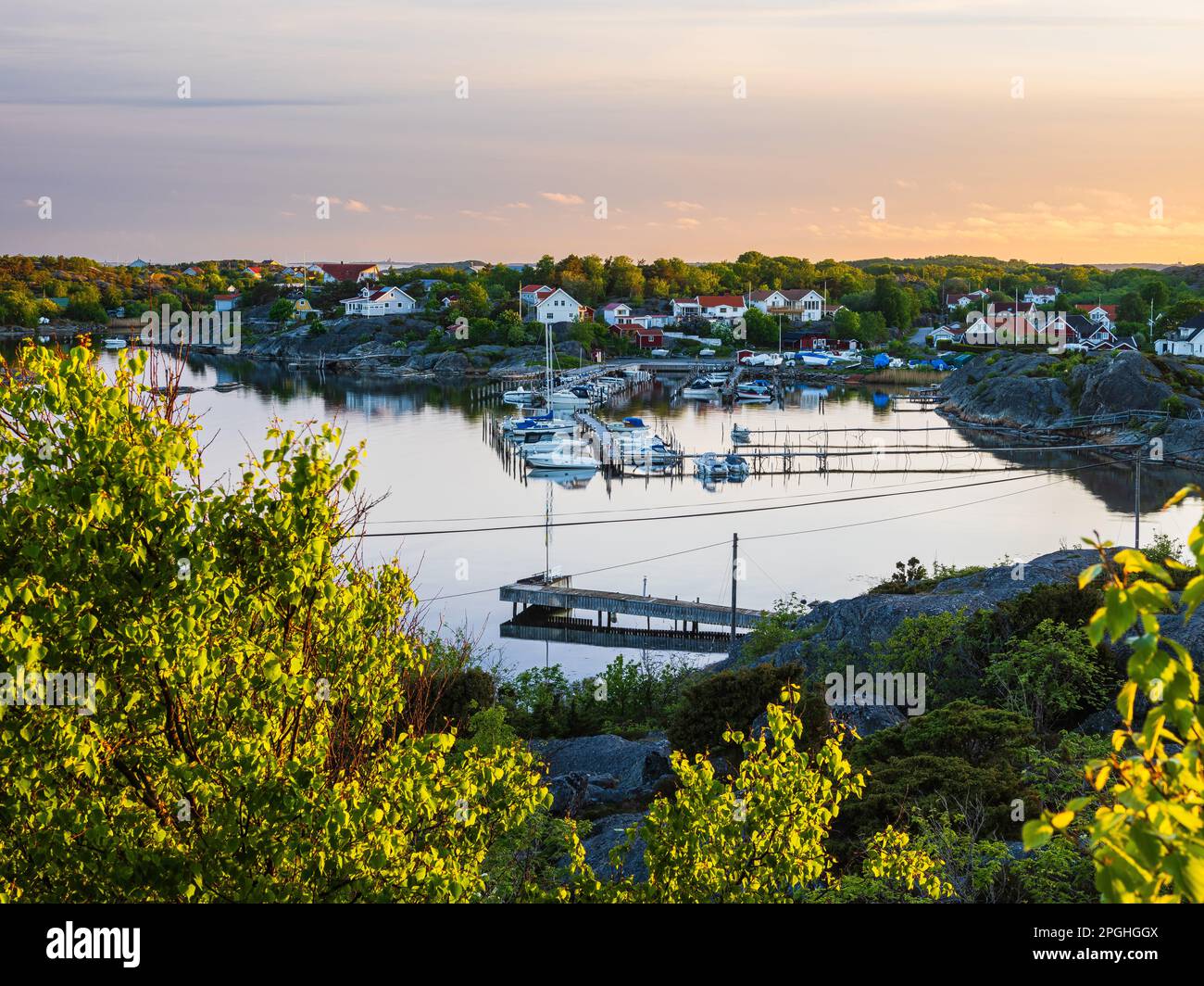 Eine ruhige Sommerszene eines Hafens in Schweden, mit Booten, die friedlich am Flussufer vor dem Hintergrund üppiger Pflanzen und Gebäude ruhen. Stockfoto