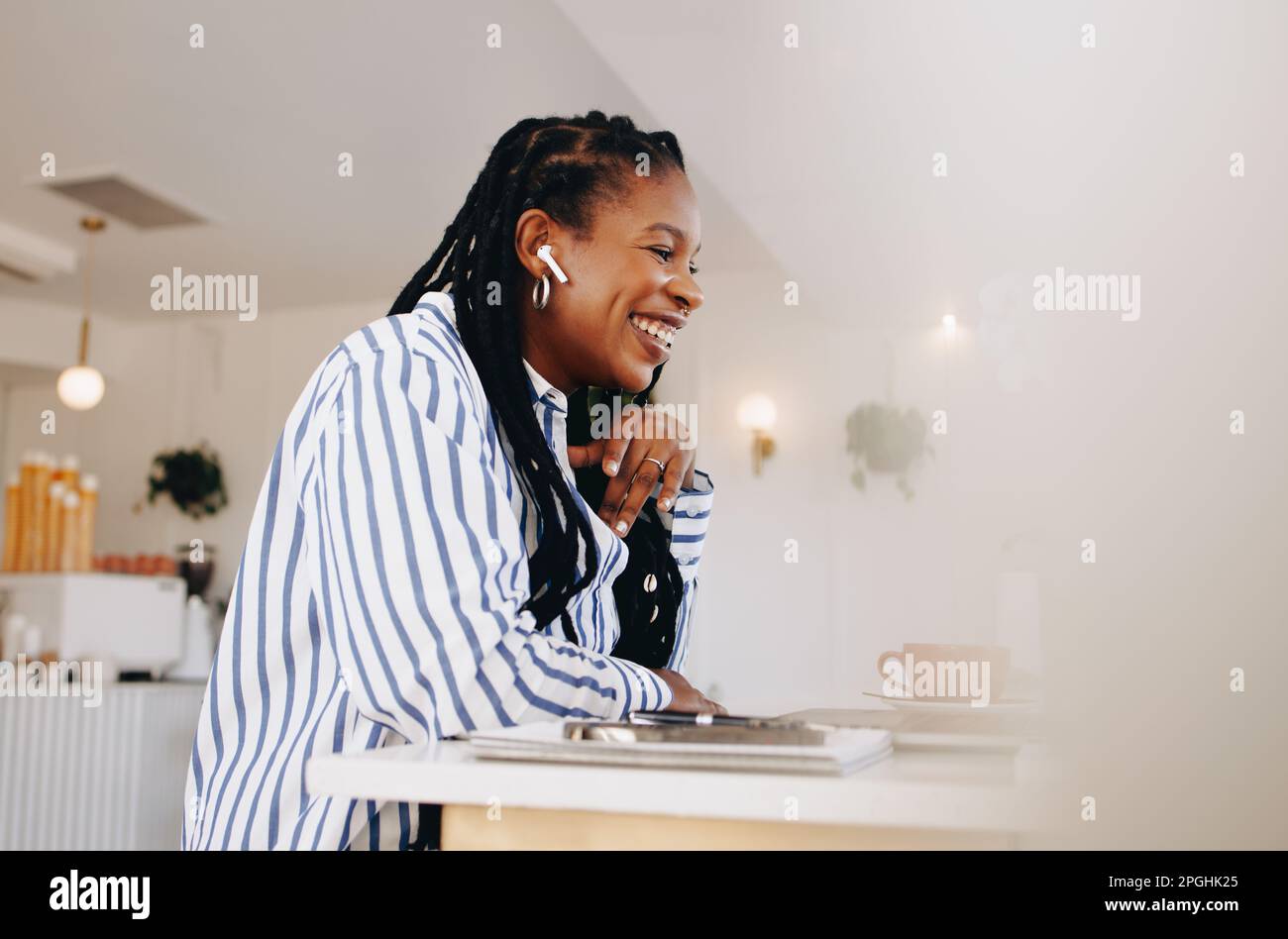 Glückliche junge Geschäftsfrau, die an einem Online-Meeting teilnimmt, während sie in einem Café arbeitet. Lächelnde junge Geschäftsfrau, die ein Gespräch mit einem Kunden führt Stockfoto