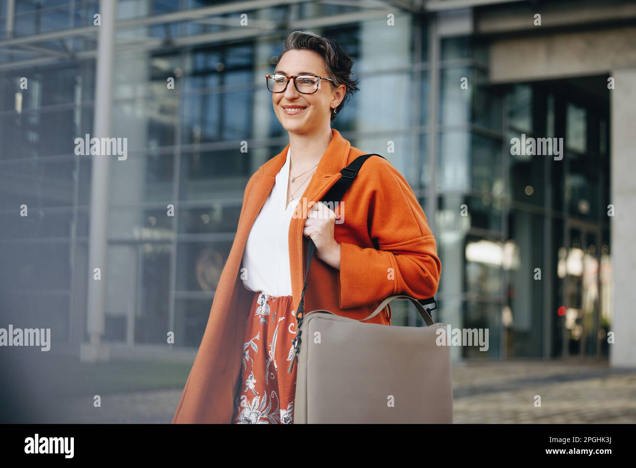 Reife Geschäftsfrau, die auf dem Weg zur Arbeit in der Stadt glücklich lächelt. Fröhliche Geschäftsfrau, die morgens zu Fuß in ihr Büro geht. Stockfoto