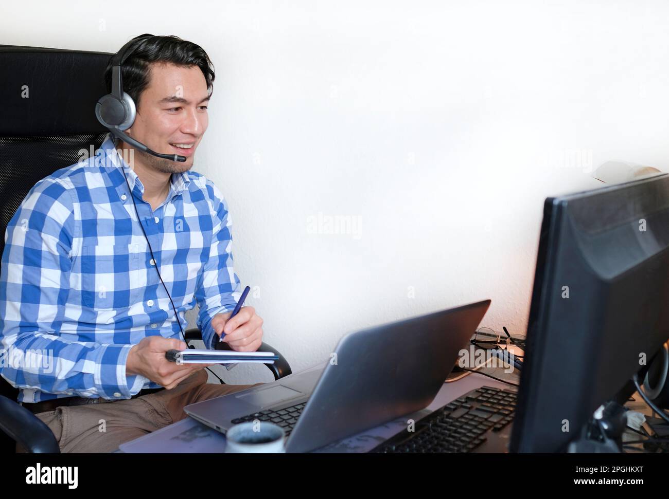 Ein Mann in einem karierten Hemd, der von zu Hause aus an einem Schreibtisch arbeitet Stockfoto