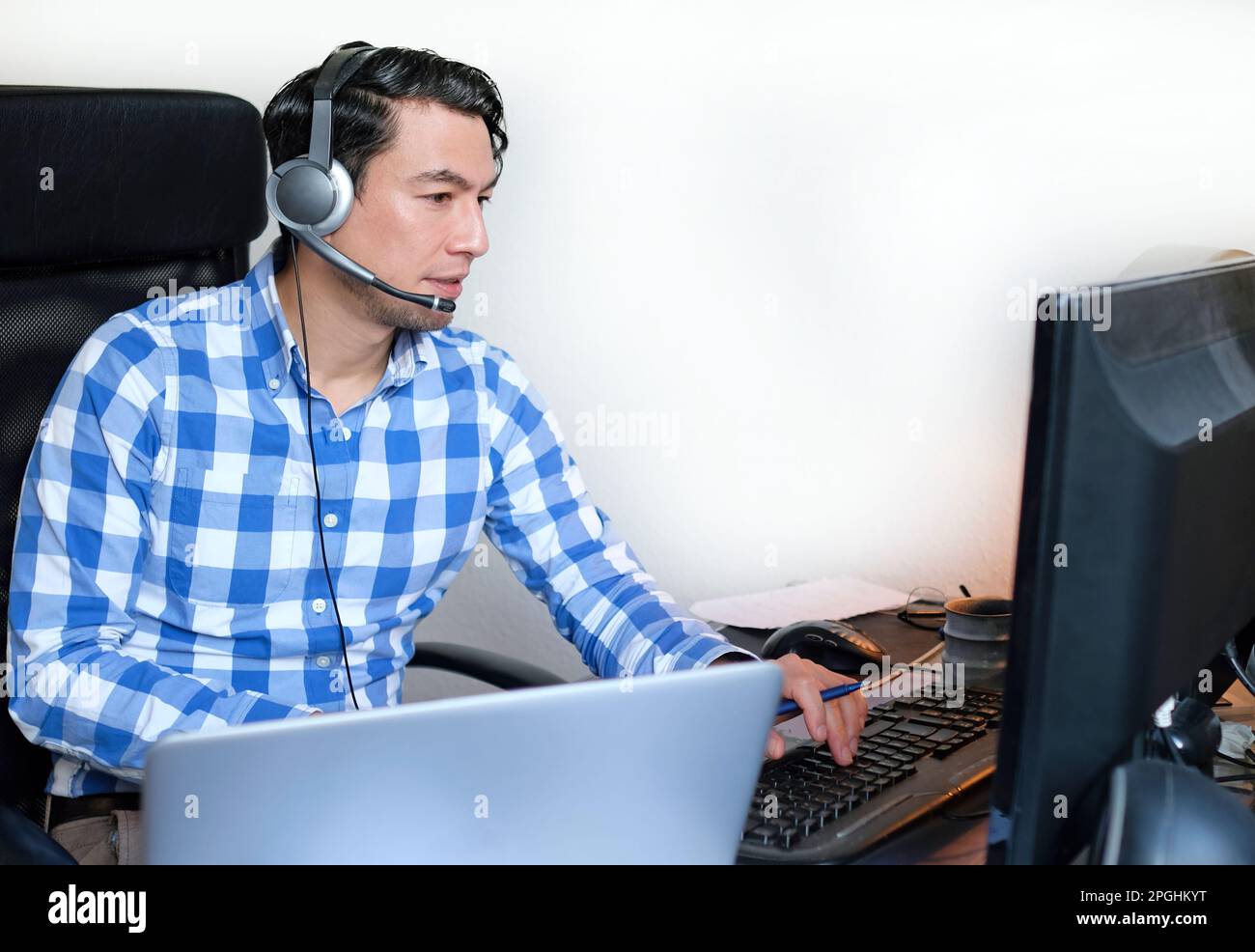 Ein Mann in einem karierten Hemd, der von zu Hause aus an einem Schreibtisch arbeitet Stockfoto