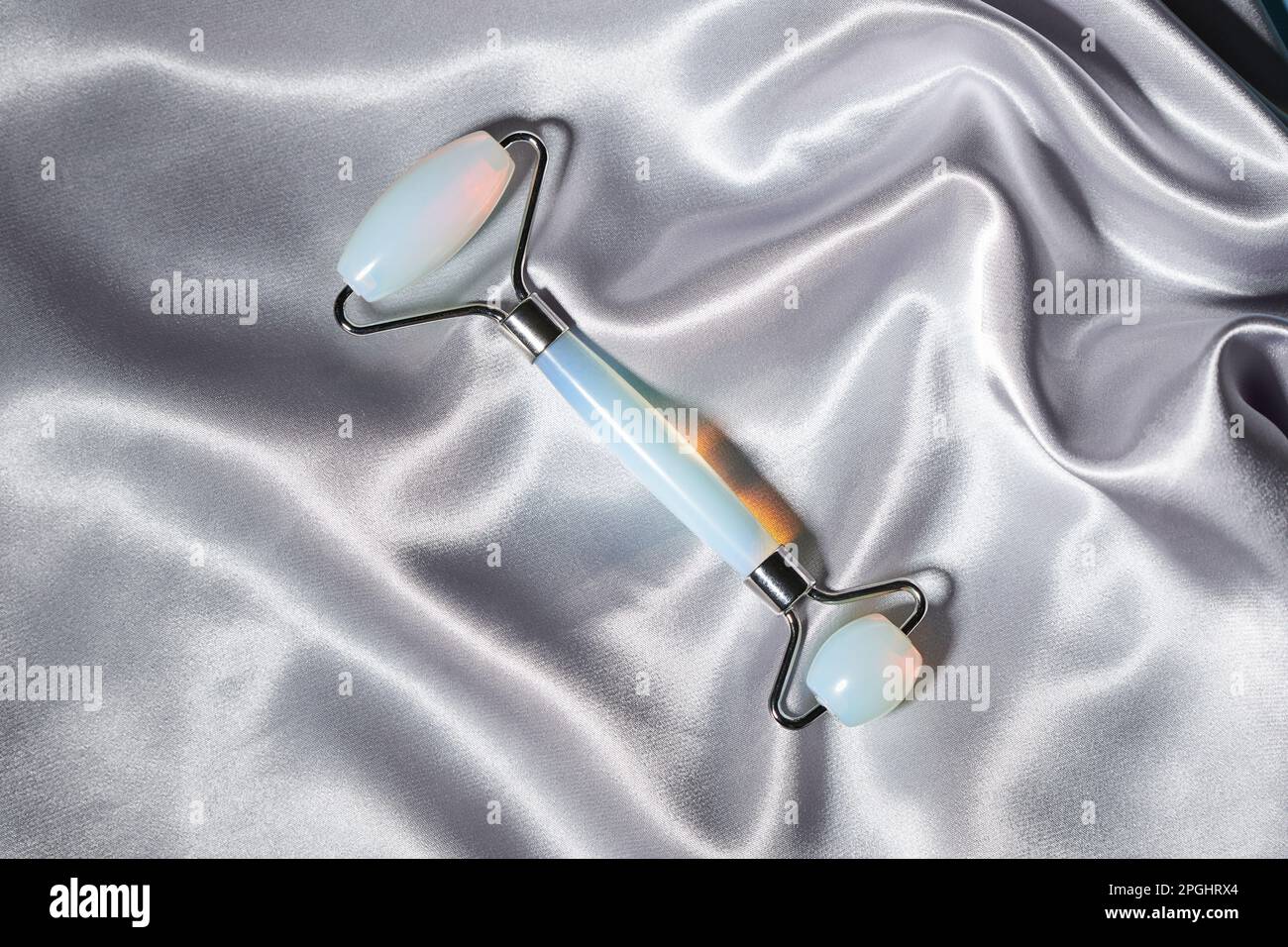 Blaue Jade-Gesichtswalze und Gua Sha-Kratzer für Schönheitsmassagen auf silbernem, strukturiertem Seidenhintergrund. Gesichtsbehandlung und Heim-Spa, Anti-agi Stockfoto