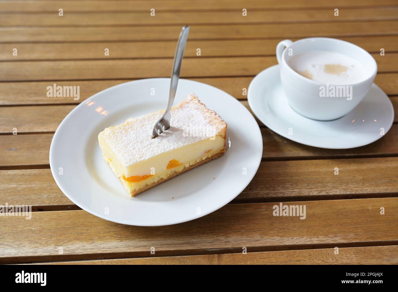 Ein Stück Käsekuchen mit Tangerinen und Puderzucker, eine Kuchengabel und eine Tasse Kaffee auf einem Holztisch im Café, Kopierraum, ausgewählter Fokus, eng Stockfoto