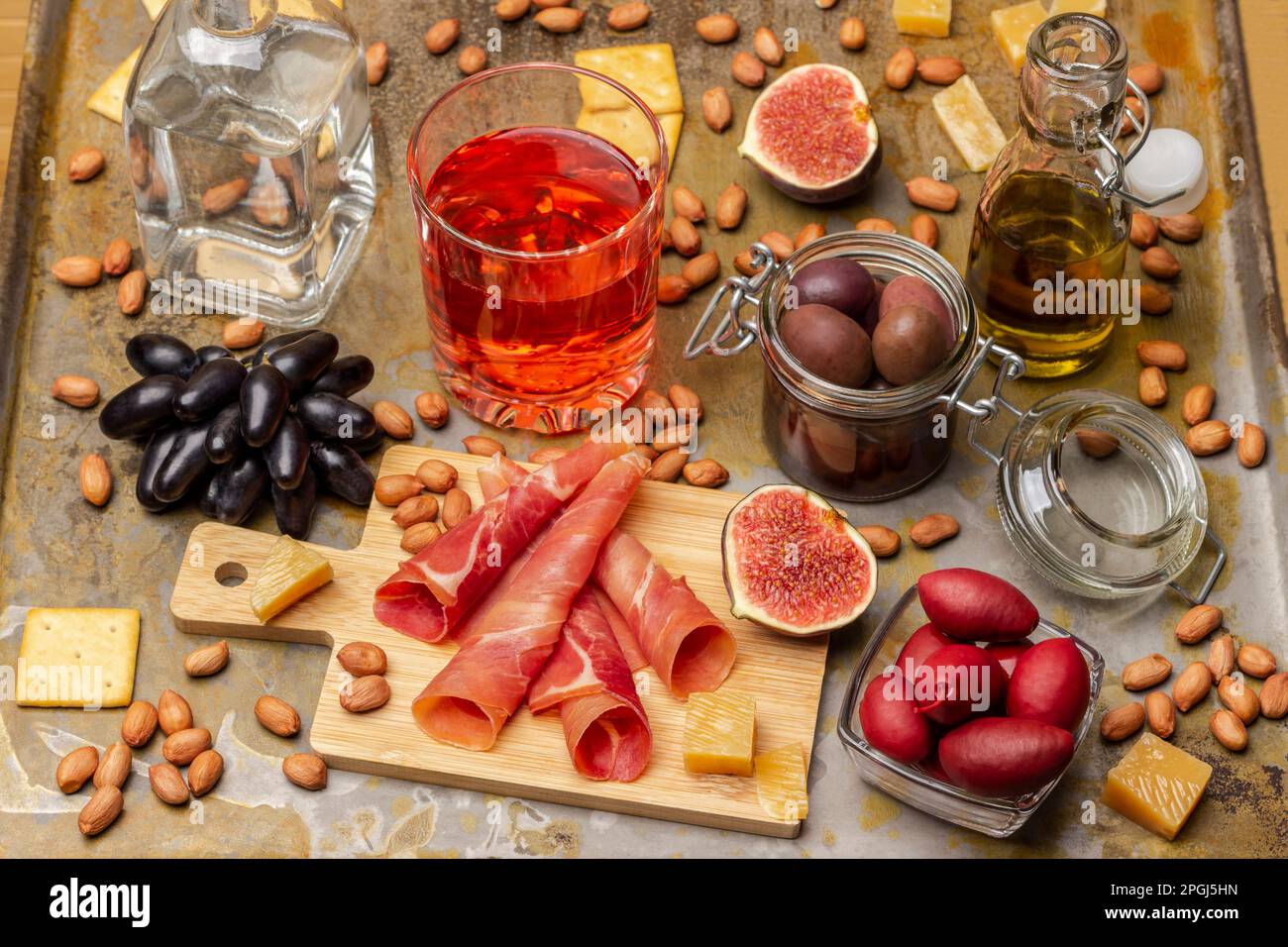 Snacks. Jamon und Feigen an Bord. Oliven in Glasgefäßen. Ein Glas Rosenwein und Traubenzweig. Nüsse und Käse. Rostiger Hintergrund. Stockfoto