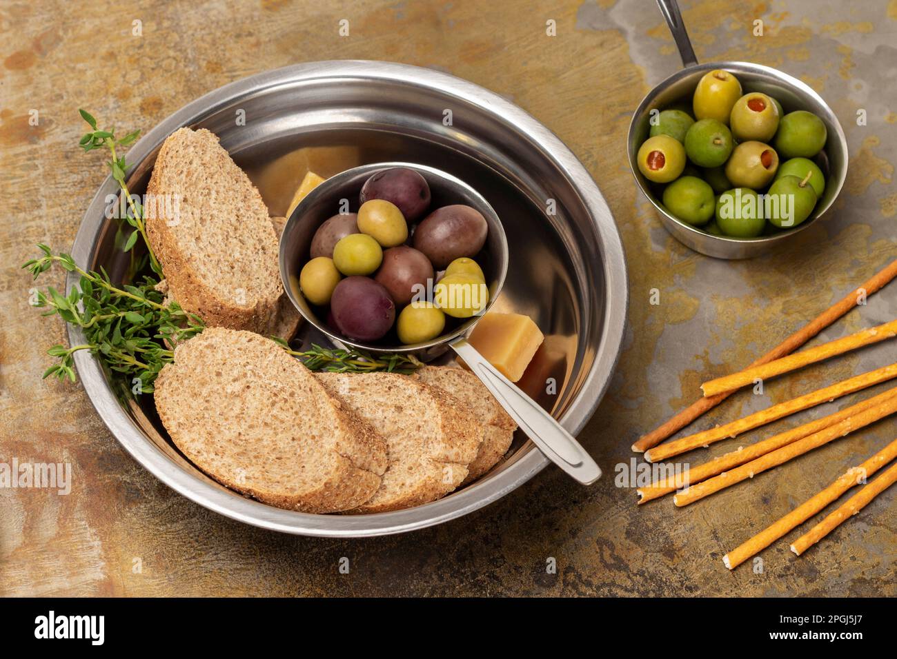 Dunkle Oliven und Baguettstücke in einer Metallschüssel. Grüne Oliven in einer Schüssel. Flach verlegt. Rostiger Hintergrund Stockfoto