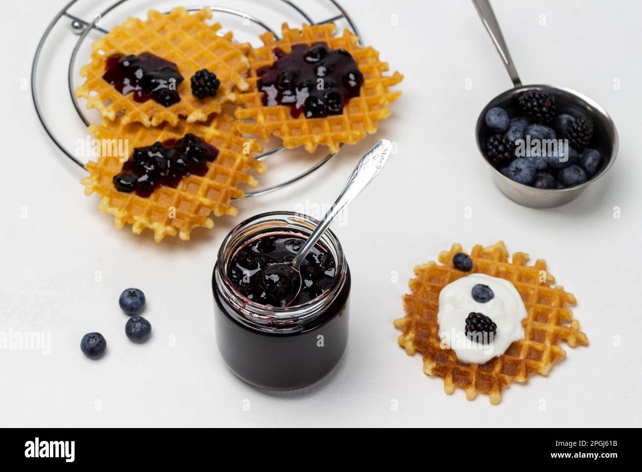 Ein Glas Marmelade. Marmelade auf Waffeln. Brombeeren und Blaubeeren in einer Metallschüssel auf dem Tisch. Weißer Hintergrund. Stockfoto
