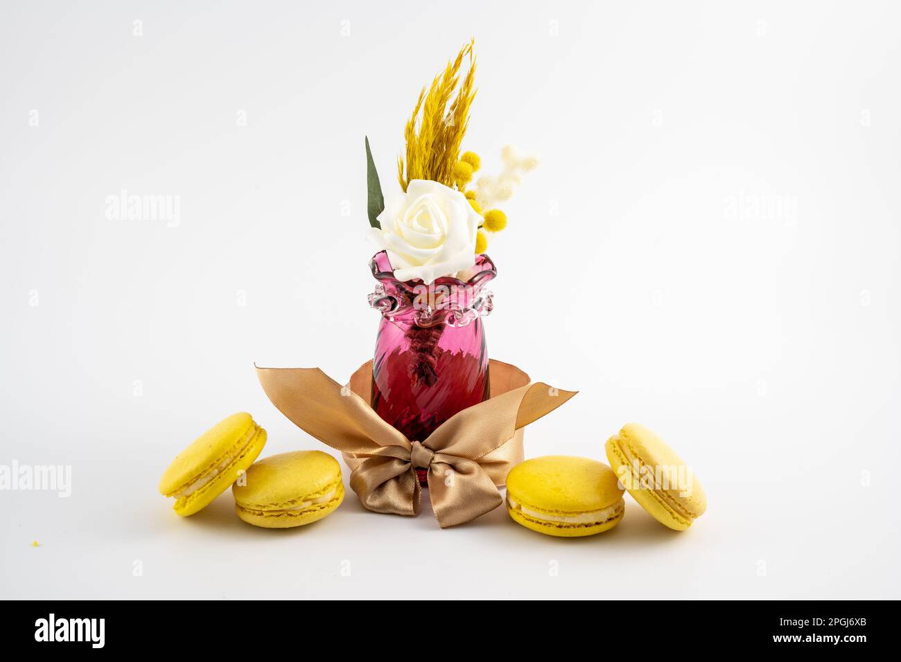 Antike rote Vase mit Schleife im Blumendesign und Makronen auf weißem Hintergrund Stockfoto
