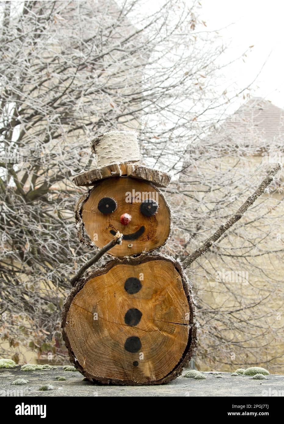 Frostiger hölzerner Schneemann mit Strohhut neben einem verschneiten Baum im Winter Stockfoto