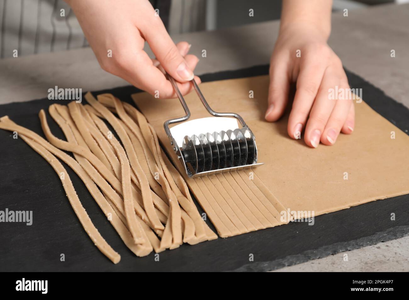 Frau schneidet Teig für Soba am Tisch, Nahaufnahme Stockfoto