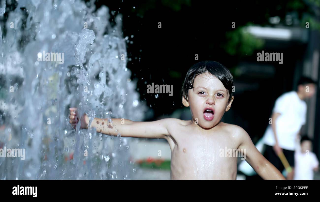 Fröhliches Kind, das Spaß bei Wasserpark Jets in 120fps Slow Motion während des heißen Sommertags hat Stockfoto