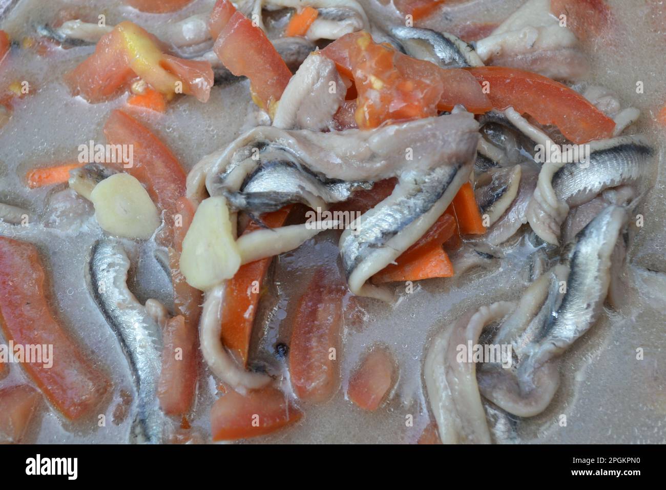 Nahaufnahme von frisch marinierten Sardellenfilets in Essig und Salz gemischt mit frischen, reifen roten Tomaten und Knoblauch als Vorspeise. Stockfoto