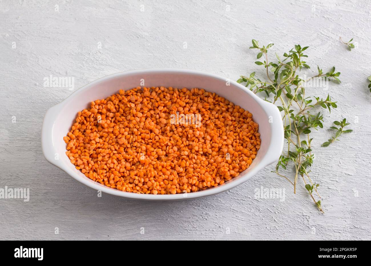 Rohe rote Linsen in einer weißen Backform mit frischem Thymian auf hellgrauem Hintergrund, Draufsicht Stockfoto