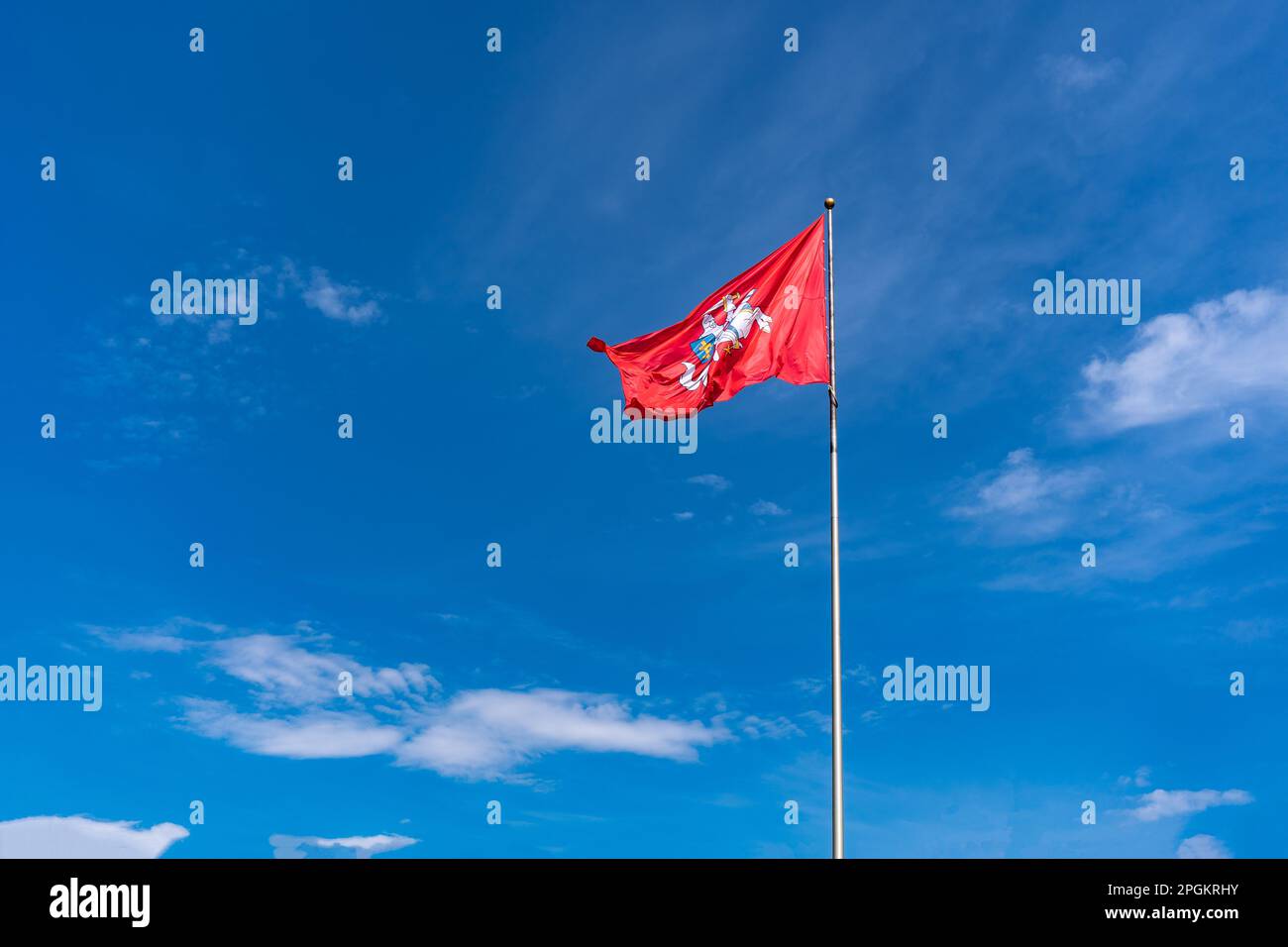 Die historische Flagge Litauens, ein Reiter mit einem Schwert auf einem weißen Pferd auf rotem Hintergrund flattert vor einem hellblauen Himmel mit weißen Wolken Stockfoto