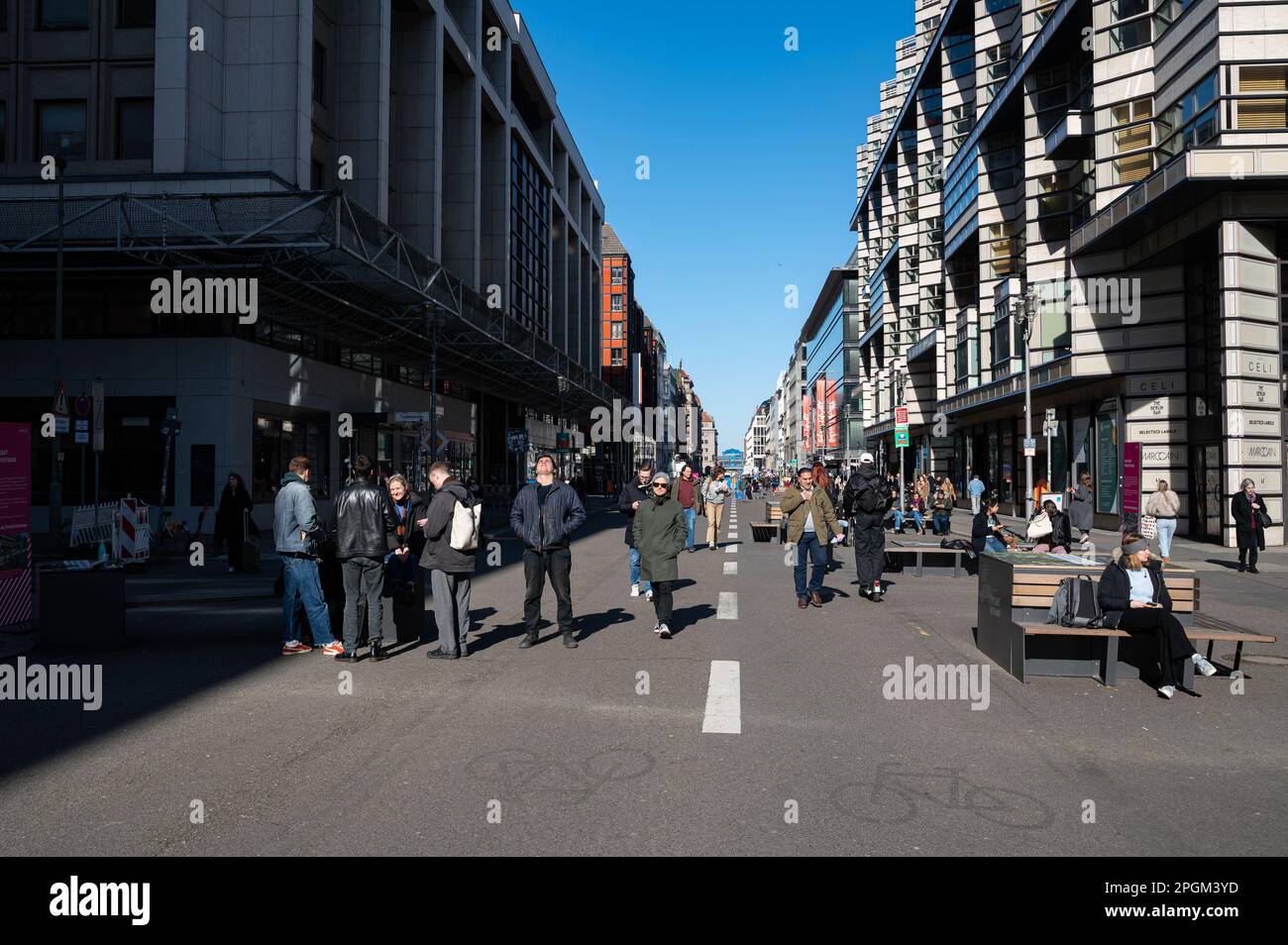 28.02.2023, Berlin, Deutschland, Europa - Fußgänger laufen entlang der autofreien Friedrichstraße im Berliner Stadtteil Mitte, vorbei an Leuten, die auf Bänken sitzen. Stockfoto
