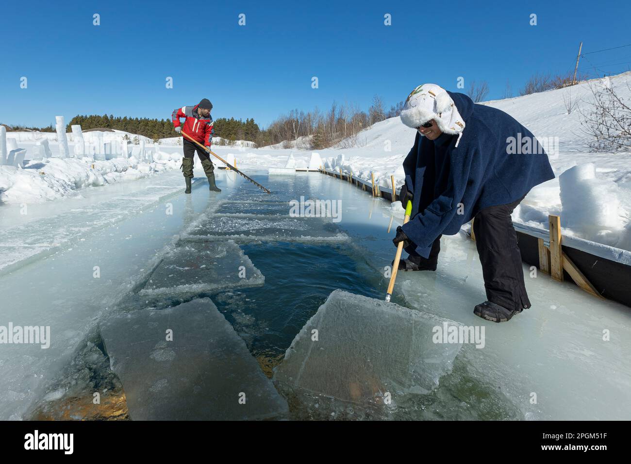 Martin Brunet verwendet eine Eissäge, während Ricardo Pan Neves das Eis aus einem See zieht, bevor Eisschwimmer ein Bad im kalten Wasser südlich von Quebec City nehmen. 12. März 2023. Stockfoto