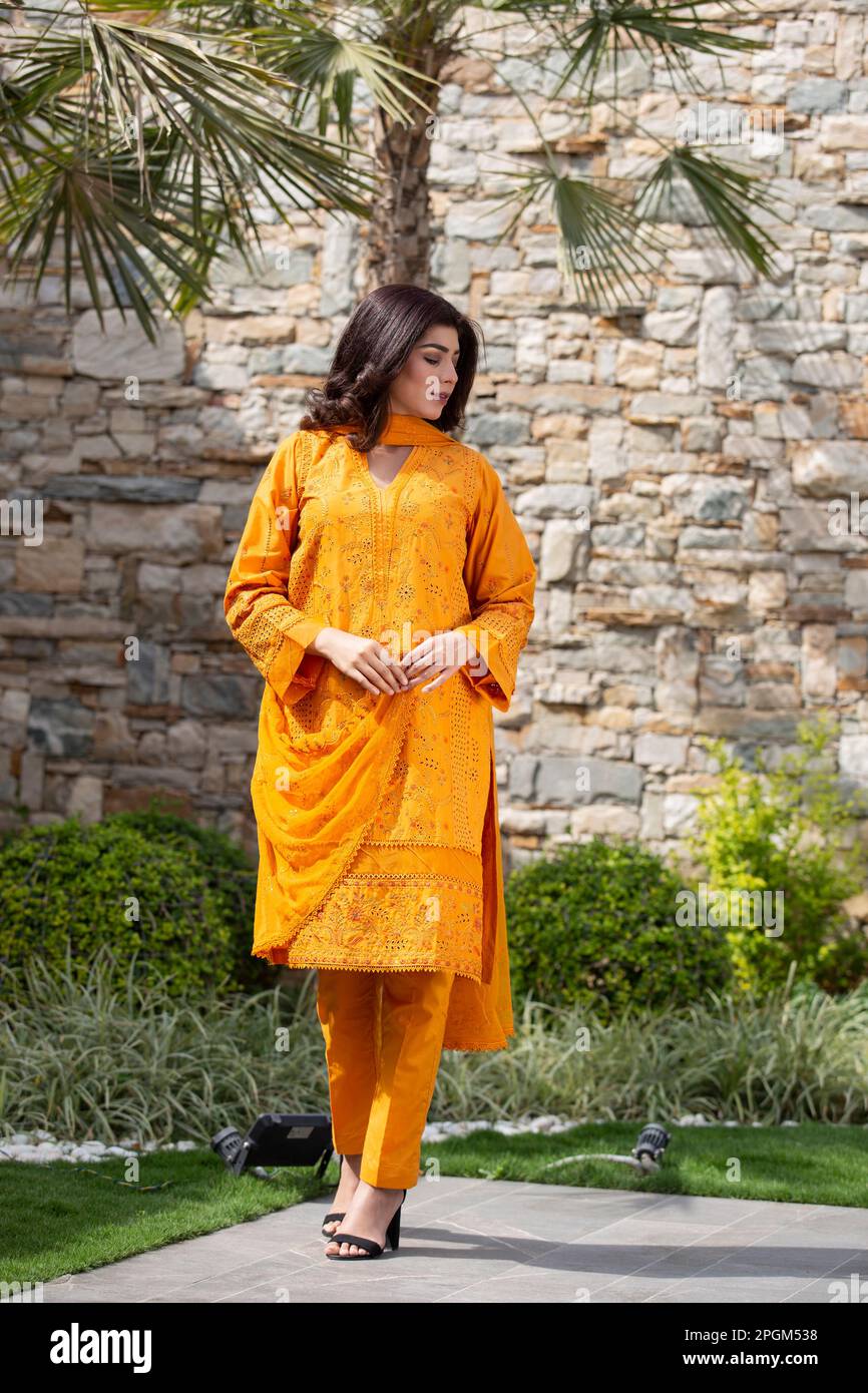 Weibliches Model, das draußen posiert und orangefarbene indische pakistanische asiatische traditionelle Salwar-Kameez trägt, Stockfoto