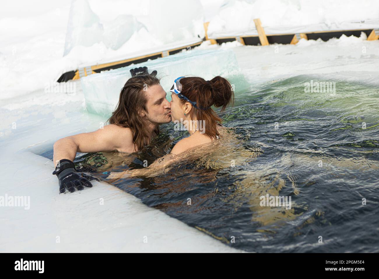 Maxime Mireault und Manon Levesque küssen sich, während sie am 5. März 2023 in das kalte Wasser eines gefrorenen Sees südlich von Québec schwimmen. Stockfoto