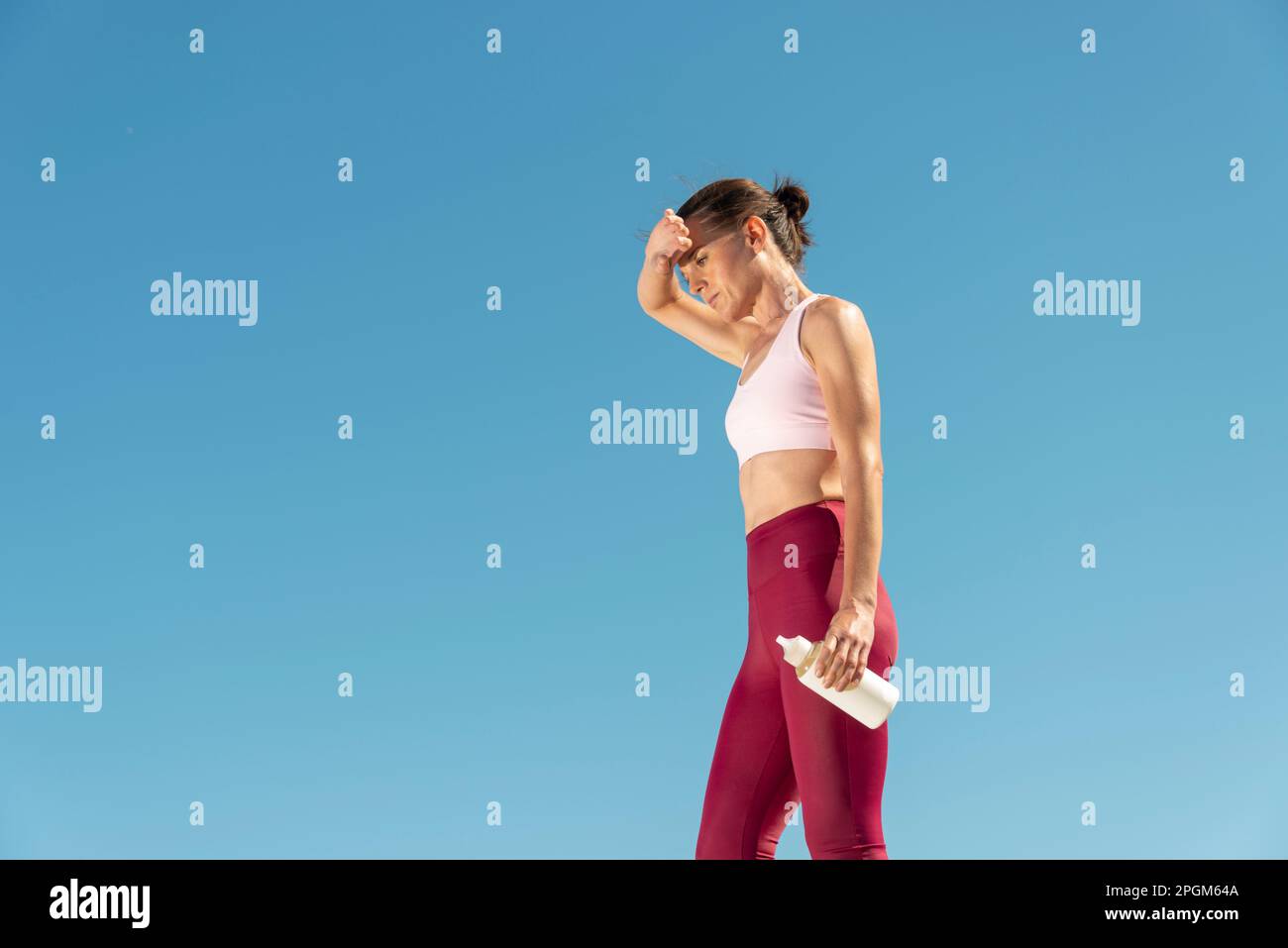 Fit sportliche Frau steht in der Sonne und hält eine Glasflasche Wasser, Hitzewelle Konzept. Stockfoto