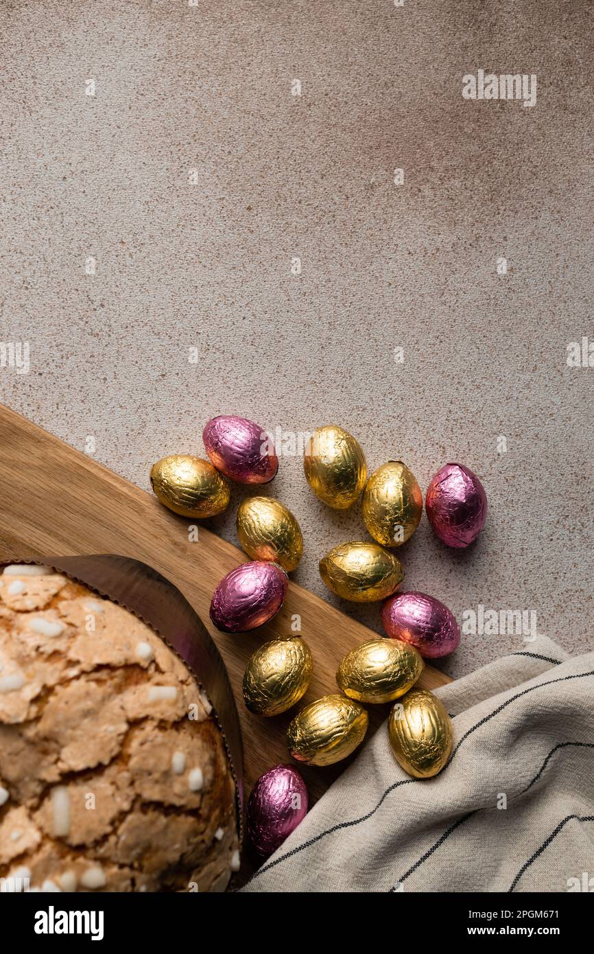 Ostertaubenkuchen oder Brot kulich mit Schokolade Ostereiern, Holzbrett, gestreifte Serviette auf Betonhintergrund. Vertikal, für Rezept platzieren Stockfoto