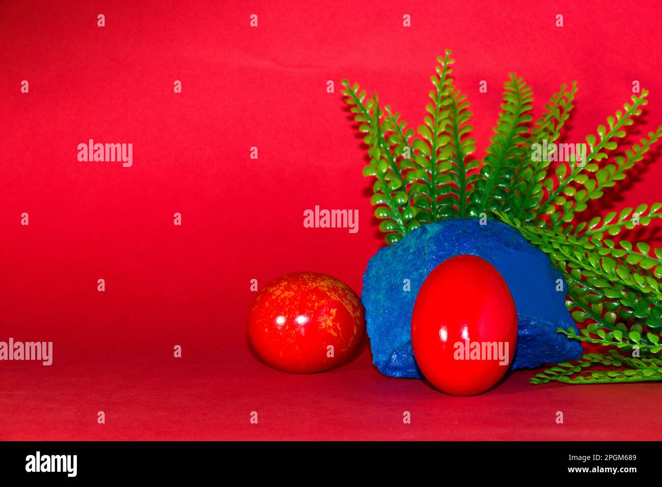 Rotes Ei auf blauem Stein mit pflanzlichem, kreativem Weihnachtsdesign auf rotem Hintergrund Stockfoto