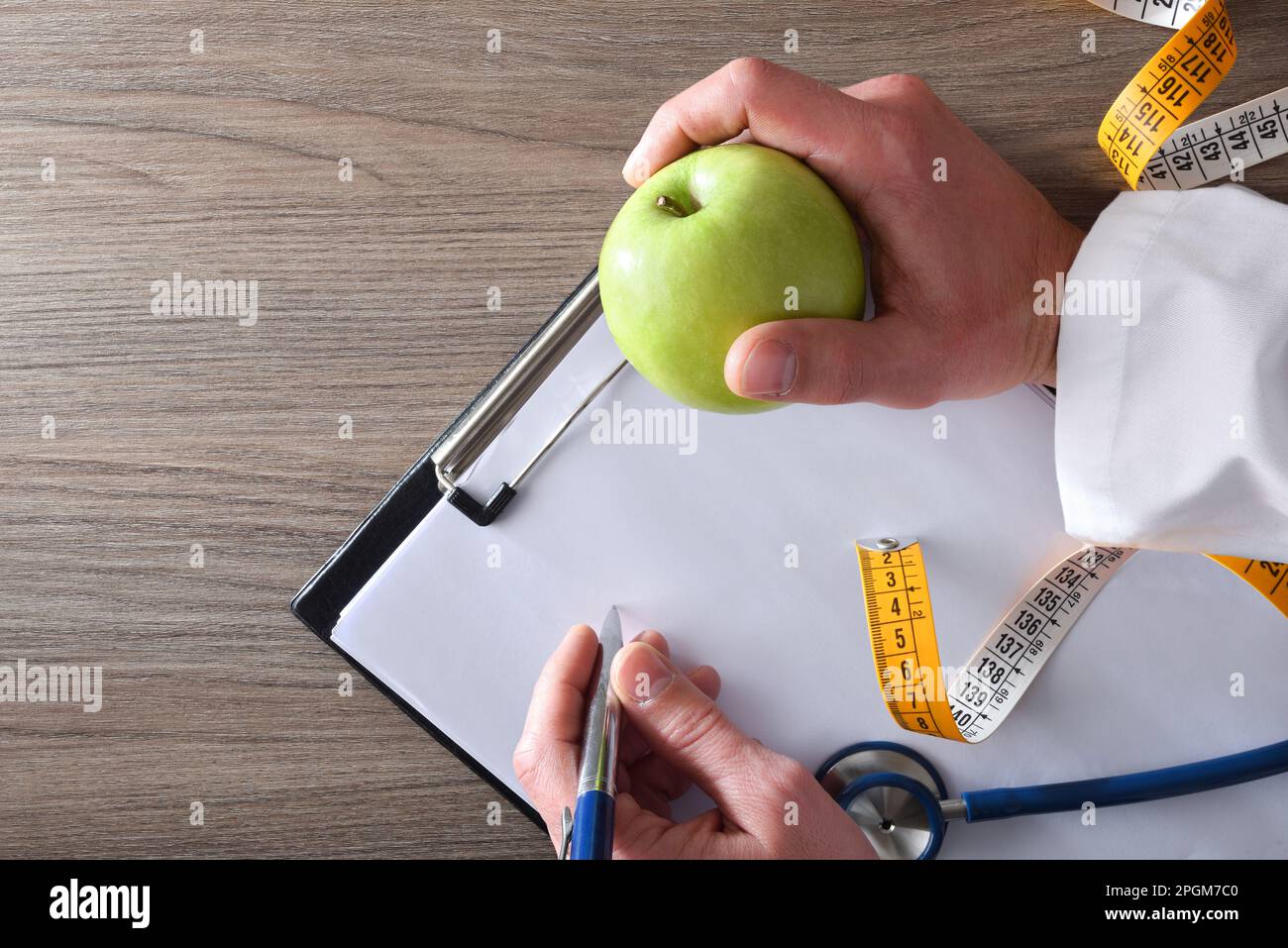 Ernährungswissenschaftler-Arzt macht sich mit Apfel in der Hand Notizen für den Bodycheck mit Stethoskop und Messgerät auf Holztisch. Draufsicht. Stockfoto