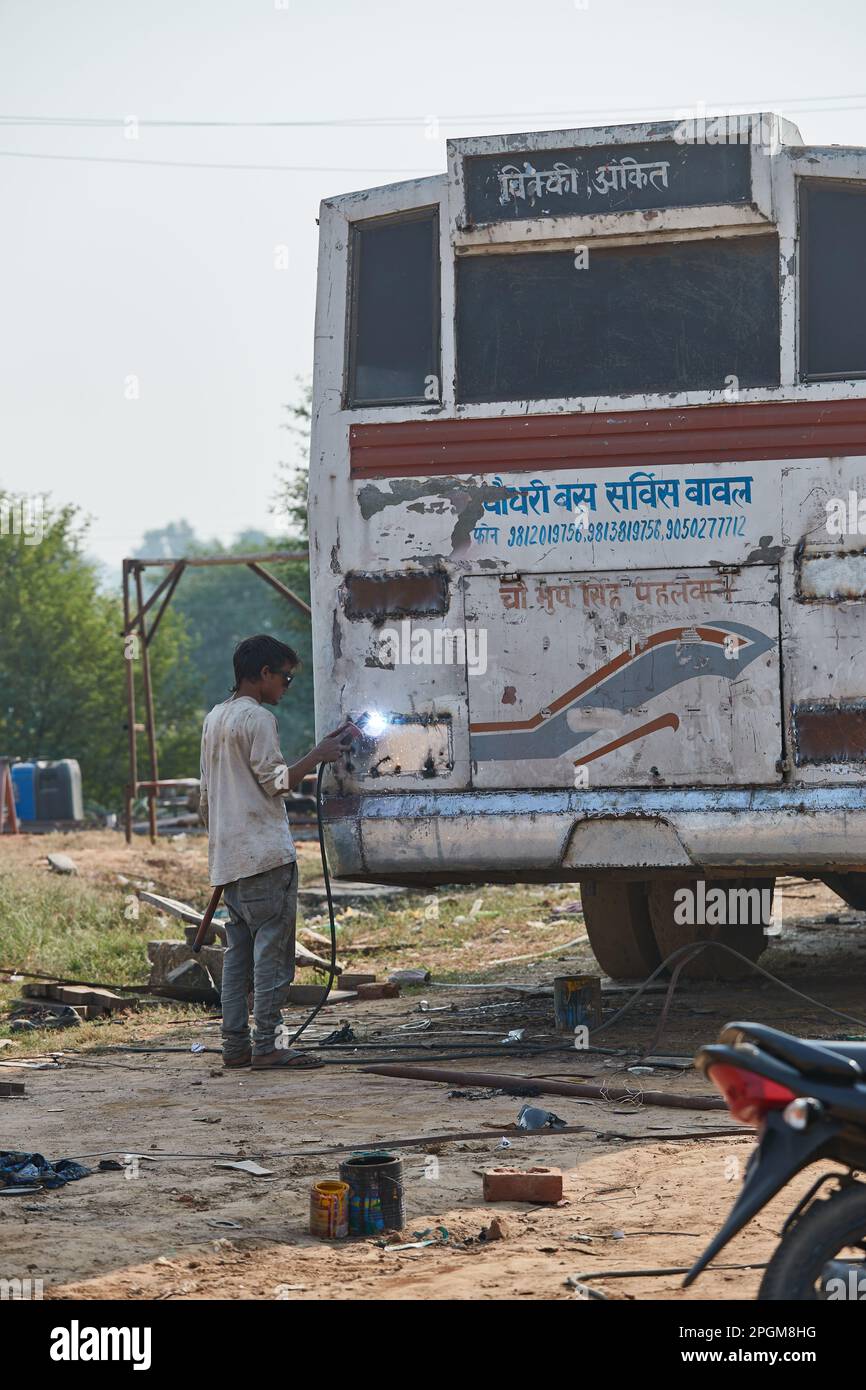 Delhi, Indien - ein Teenager, der an der Rückseite eines Busses schweißt Stockfoto