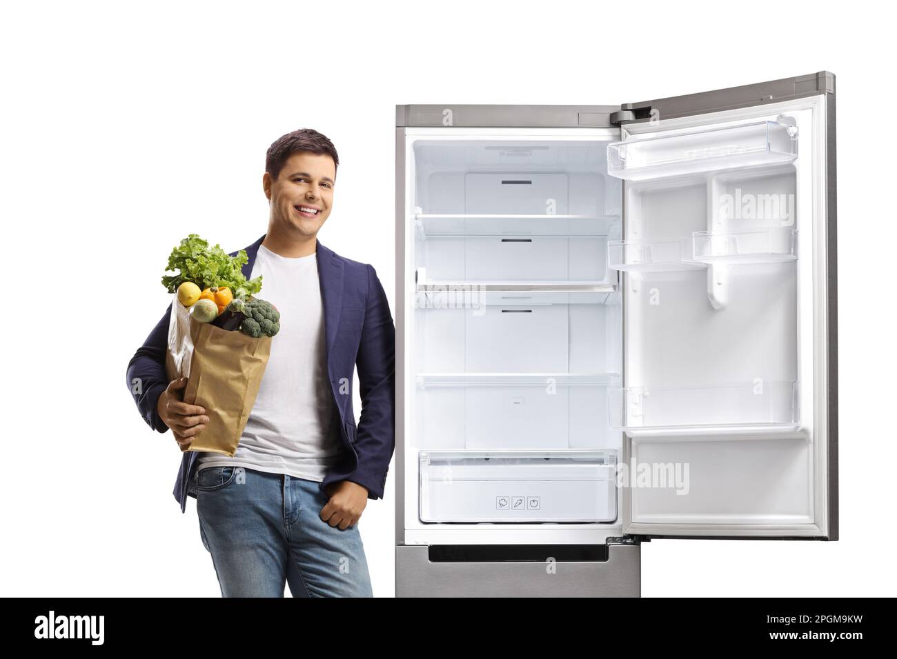 Ein junger Mann, der einen Einkaufstasche in der Hand hält und sich auf einen Kühlschrank lehnt, isoliert auf weißem Hintergrund Stockfoto