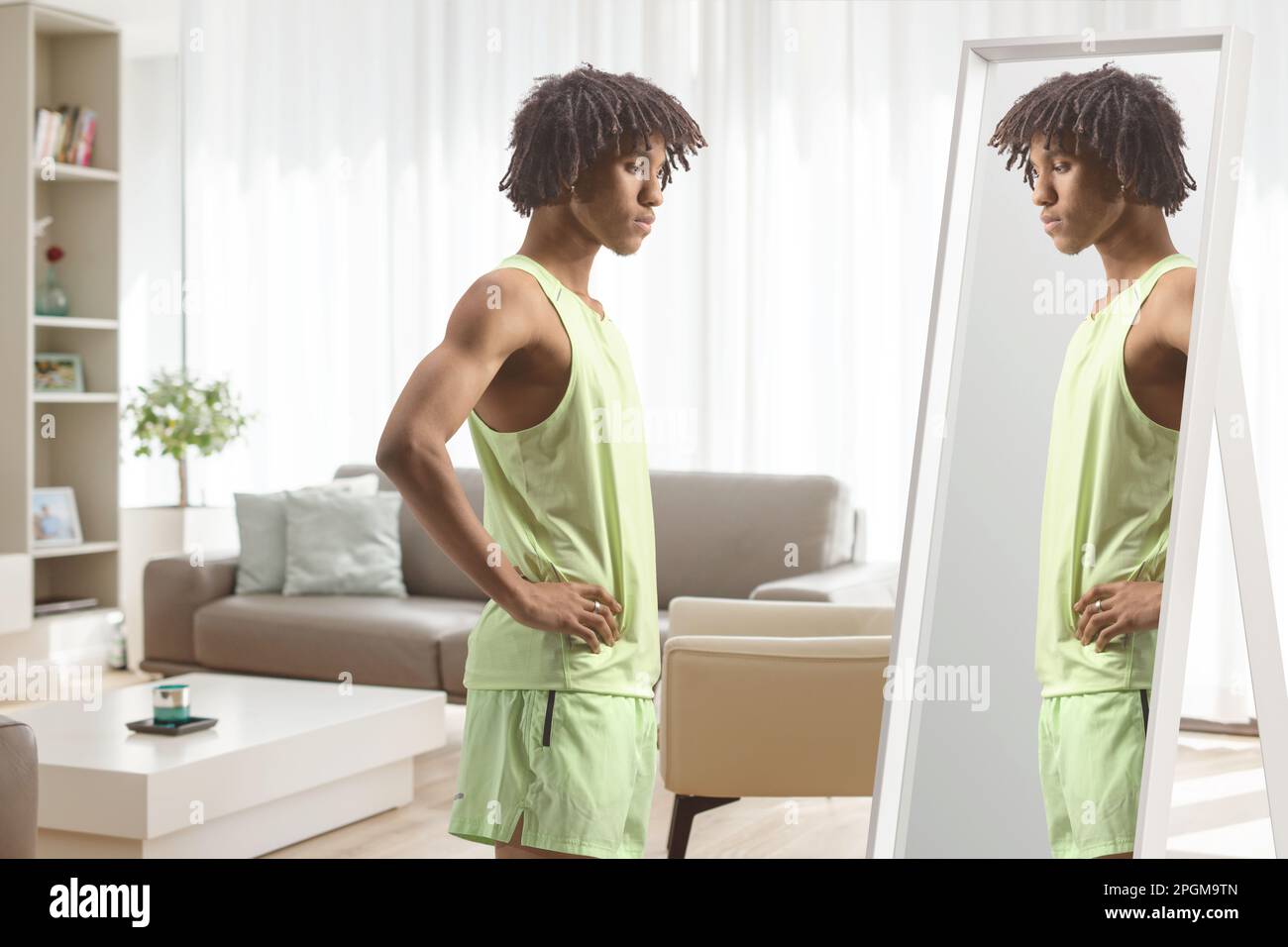 Ein junger afroamerikanischer Mann in Sportbekleidung, der in einem Wohnzimmer in einen Spiegel schaut Stockfoto