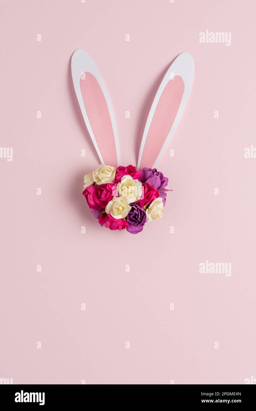 Hasen- oder Kaninchenohr mit Frühlingsblumen auf pastellrosa Hintergrund. Frohes Ostern-Minimalkonzept. Flach verlegt. Stockfoto