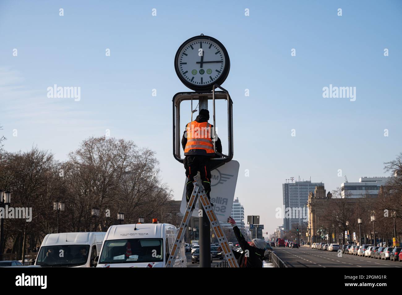 08.02.2023, Berlin, Deutschland, Europa - Arbeitnehmer wechseln die Plakate unter einer Uhr an der 17. Juni Straße als Symbol für die Sommerzeit. Stockfoto