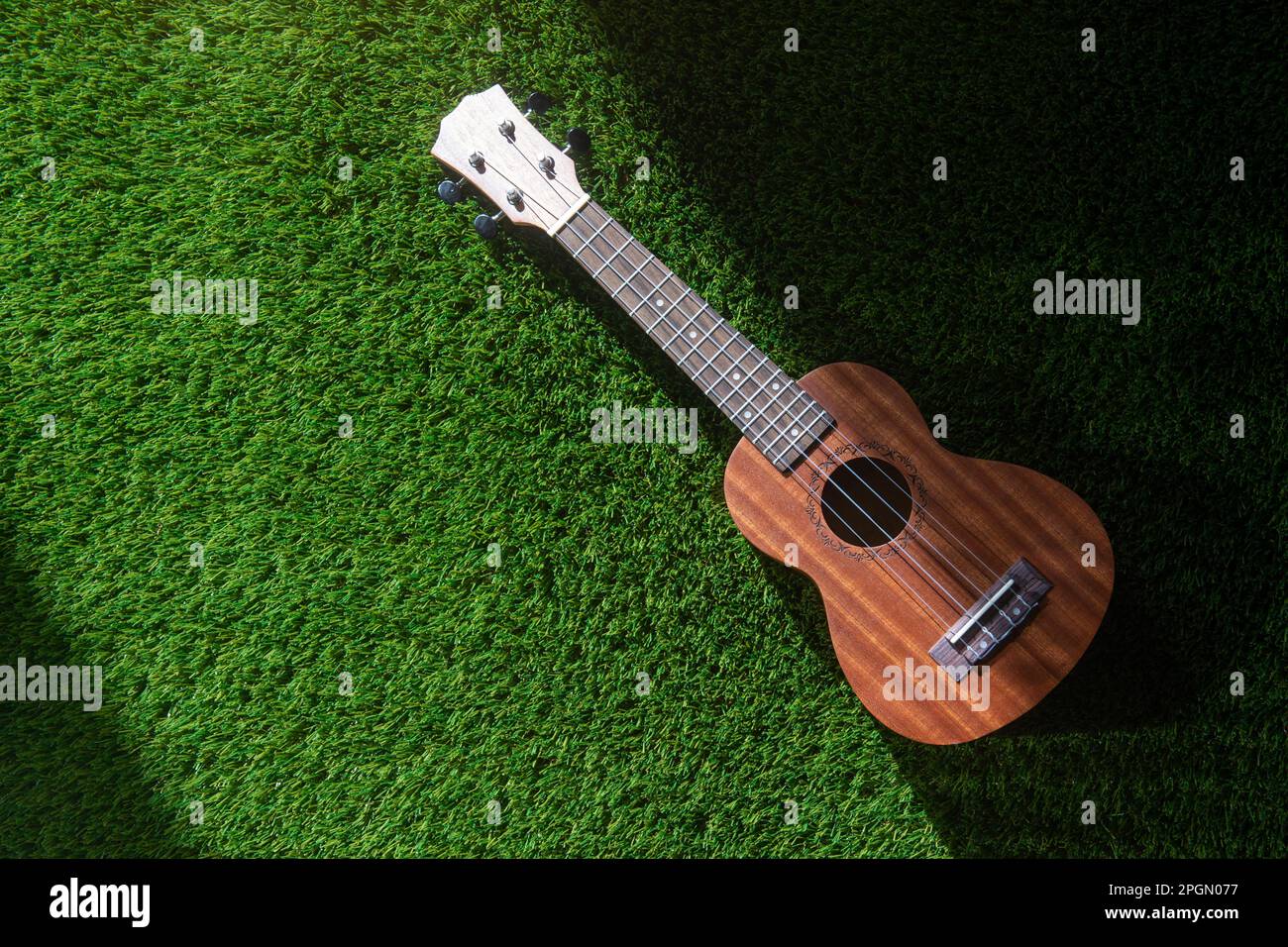 Ukulele auf grünem Gras mit Tageslicht. Horizontales Poster mit Musikmotiven, Grußkarten, Kopfzeilen, Website und App Stockfoto