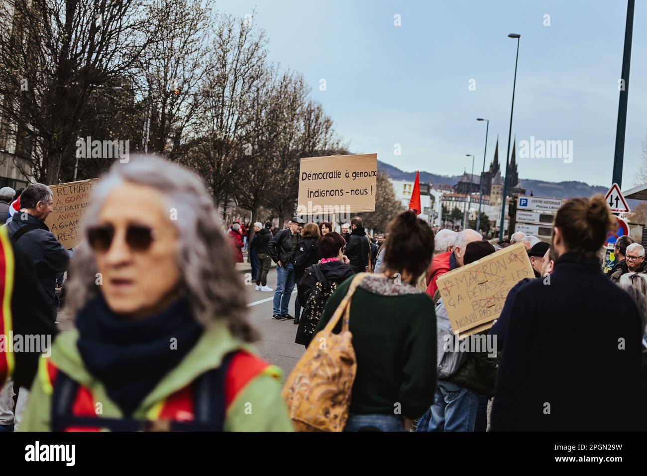 23. März 2023, Clermont Ferrand, Auvergne Rhone Alpes, Frankreich: Im Hintergrund hält eine Person ein Schild mit der Aufschrift Demokratie auf den Knien, lassen Sie uns empört sein! Frankreich streikt erneut gegen die zutiefst unpopuläre Rentenreform, die Ministerpräsident Elisabeth letzte Woche unter Verwendung von Artikel 49,3 durch das Parlament gedrängt hat. Am Mittwoch kündigte Präsident Macron im Fernsehen an, dass er sich dafür aussprach, dass die Renten noch vor Jahresende umgesetzt werden. (Kreditbild: © Adrien Fillon/ZUMA Press Wire) NUR REDAKTIONELLE VERWENDUNG! Nicht für den kommerziellen GEBRAUCH! Stockfoto