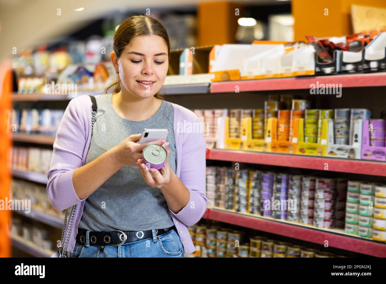 Junge glückliche Frau scannt qr-Code auf Dosenfutter in der Tierhandlung Stockfoto