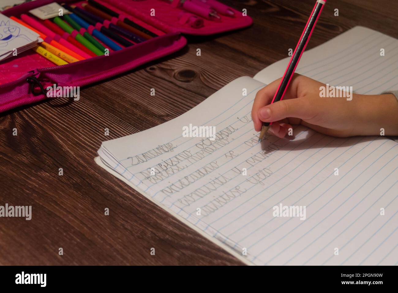 Eine junge Studentin, die mit einem Bleistift an ihrem Schreibtisch schreibt Stockfoto