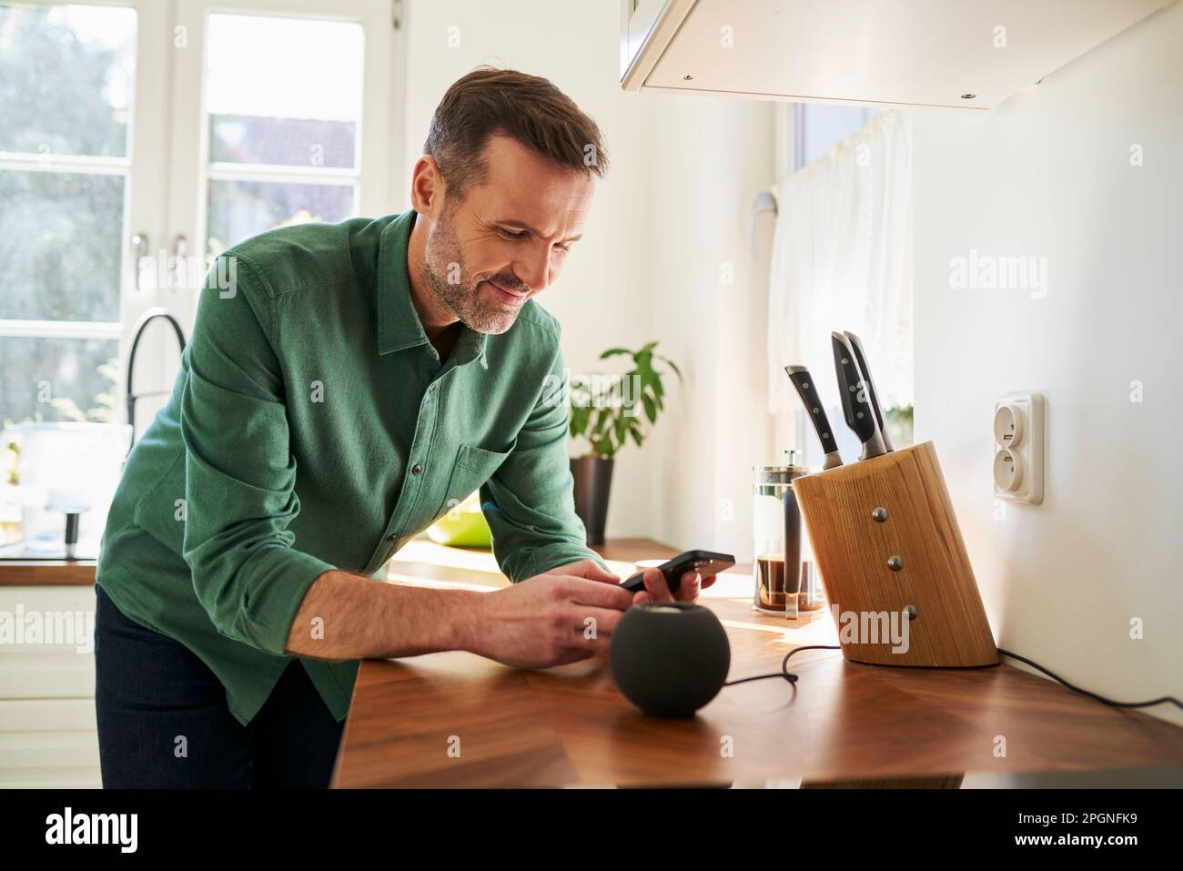 Mann, der zu Hause steht und das Smartphone mit dem Lautsprecher verbindet Stockfoto