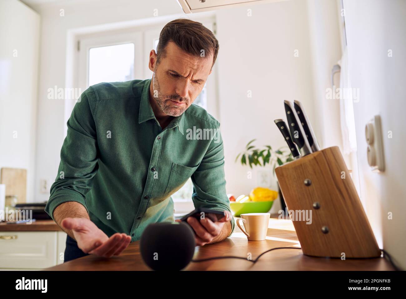 Mann, der zu Hause steht und das Smartphone mit dem Lautsprecher verbindet Stockfoto