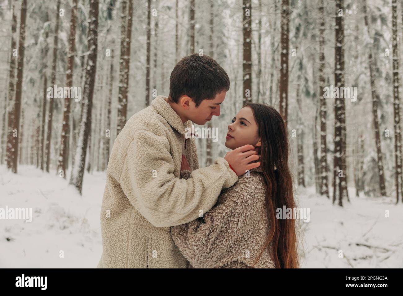 Ein romantisches Teenager-Paar, das im verschneiten Wald zusammensteht Stockfoto