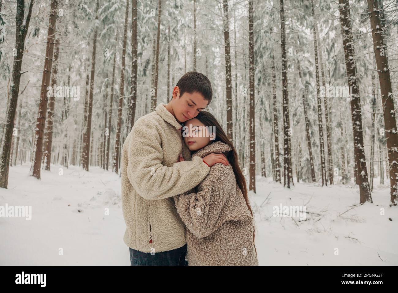 Ein Freund im Teenageralter umarmt eine Freundin im verschneiten Wald Stockfoto