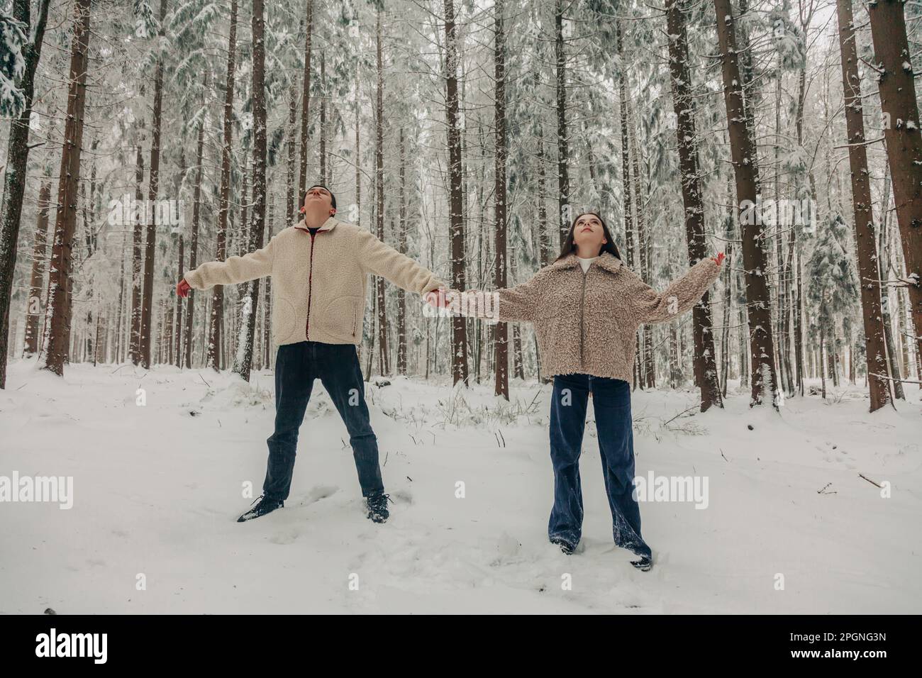 Ein Teenager-Paar, das Händchen hält und im verschneiten Wald steht Stockfoto