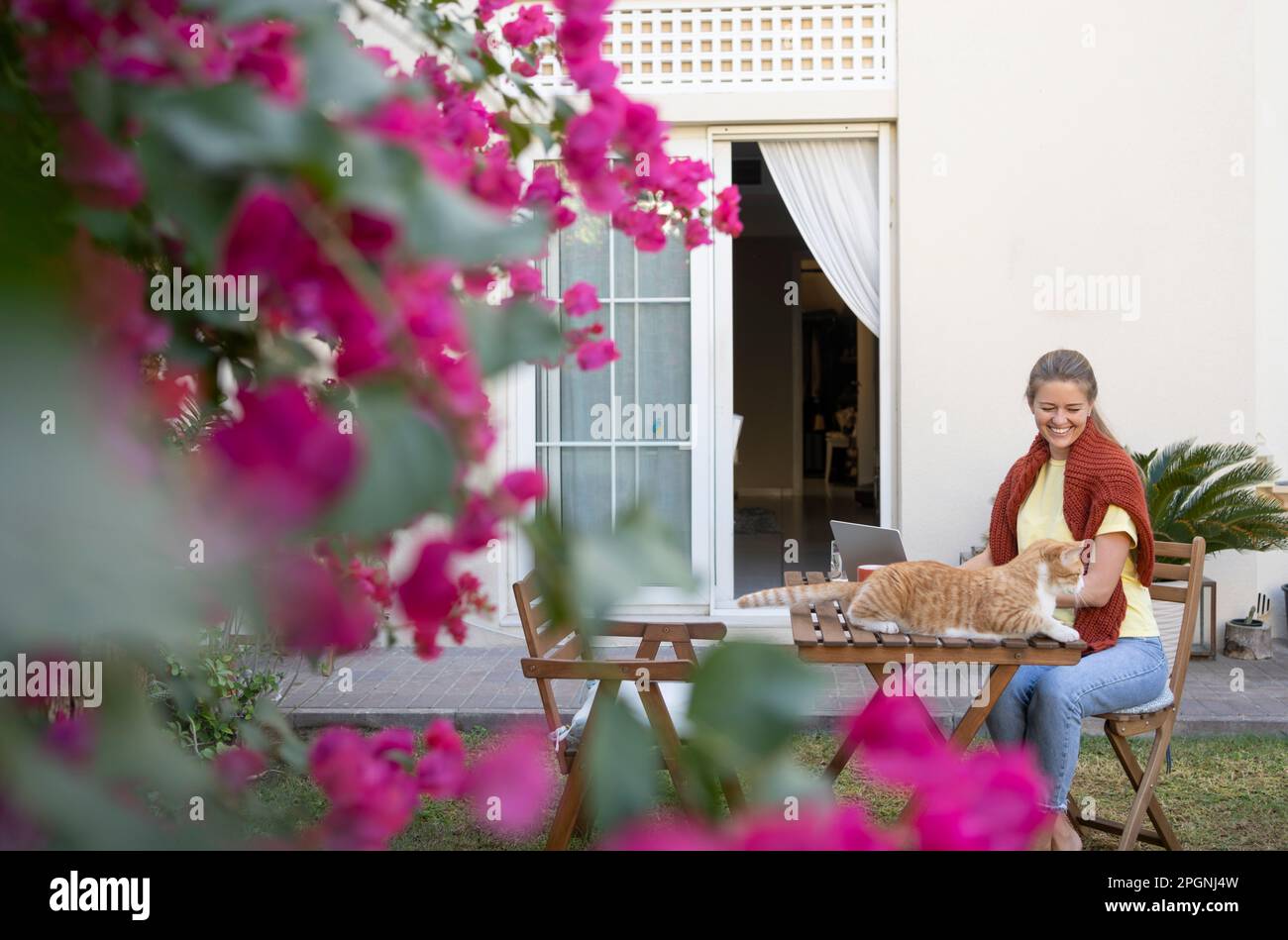 Lächelnder Freiberufler mit Hauskatze, die auf einem Stuhl im Garten sitzt Stockfoto