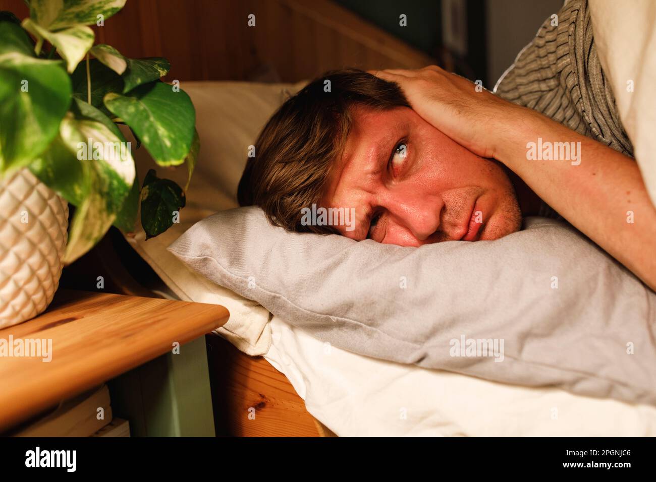 Ein Mann, der sich die Ohren zudeckt und zu Hause auf dem Bett liegt Stockfoto