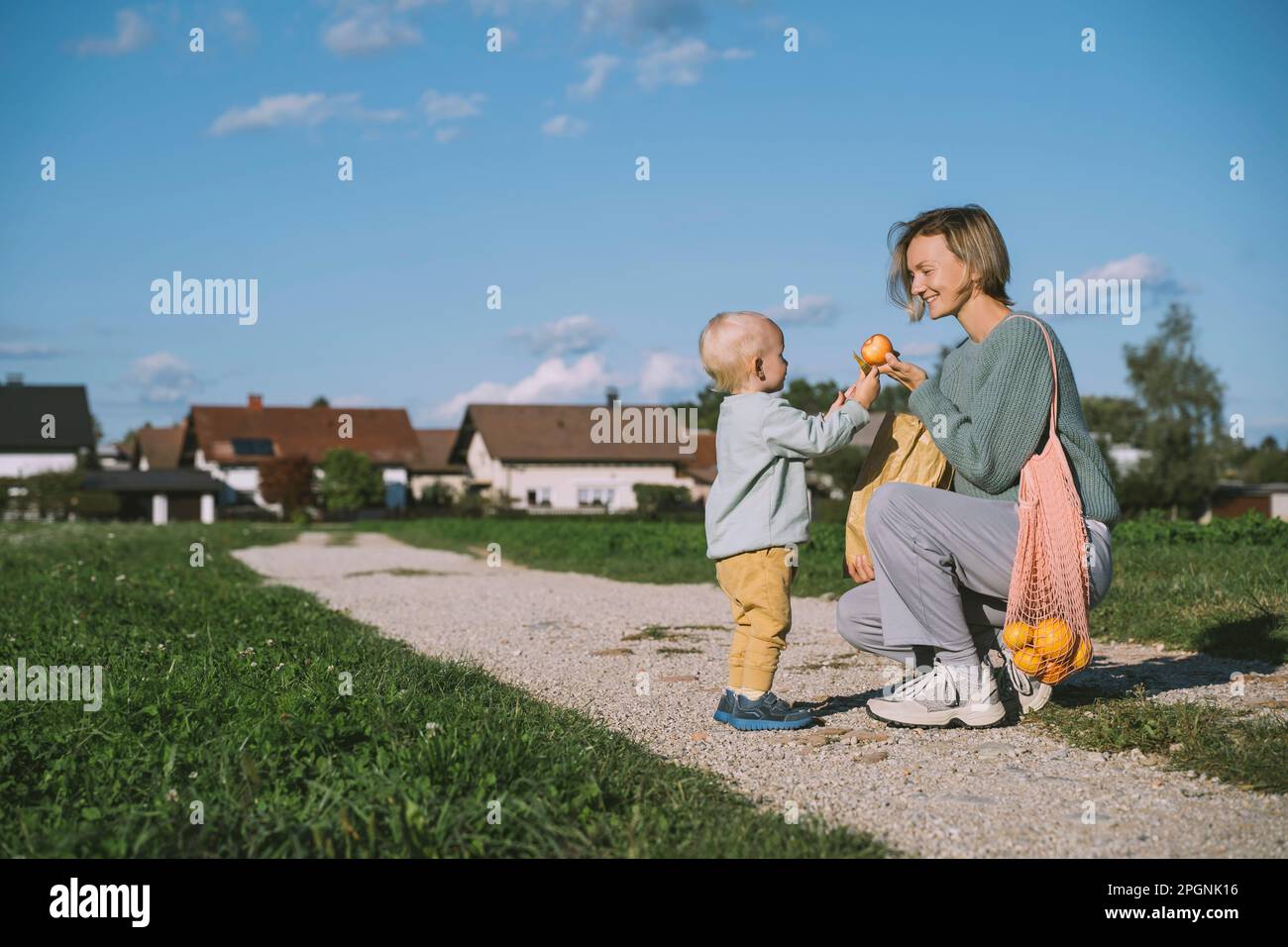 Lächelnde Frau, die dem Sohn auf dem Fußweg einen Apfel gibt Stockfoto