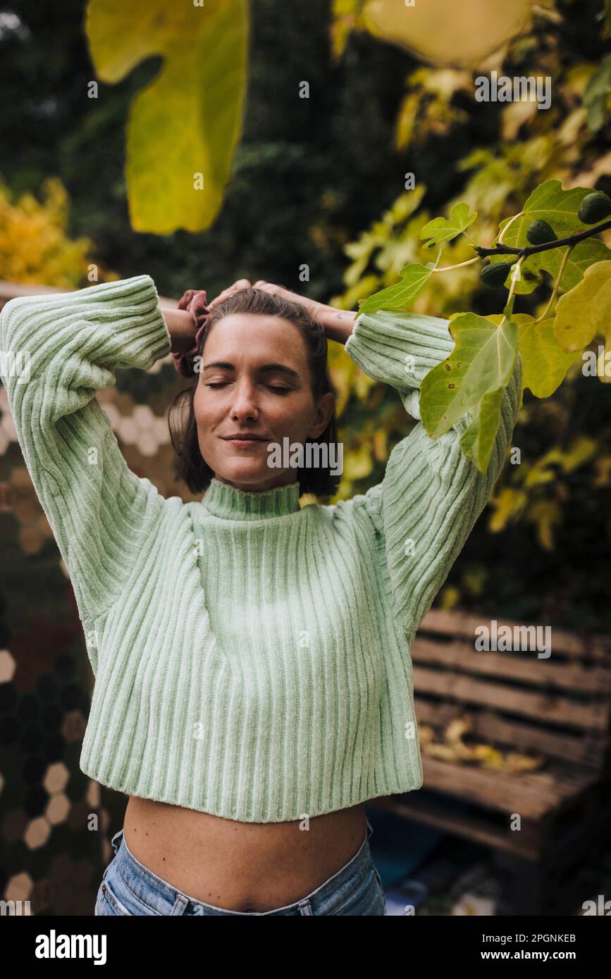 Lächelnde Frau mit Händen hinter dem Kopf, die im Garten steht Stockfoto