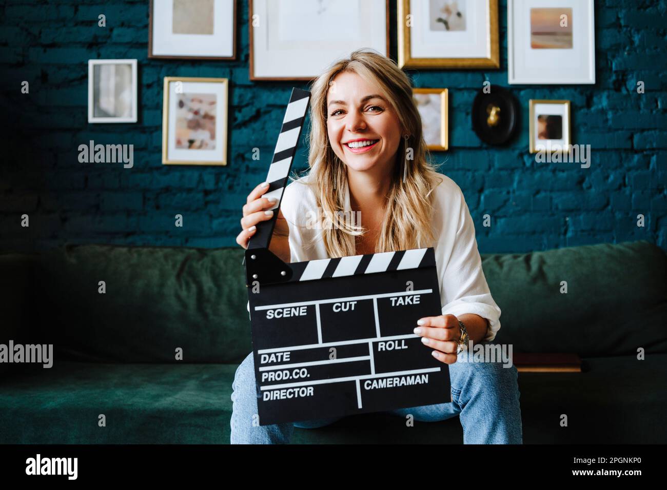 Eine glückliche Schauspielerin, die auf dem Sofa am Filmset mit dem Klappbrett sitzt Stockfoto